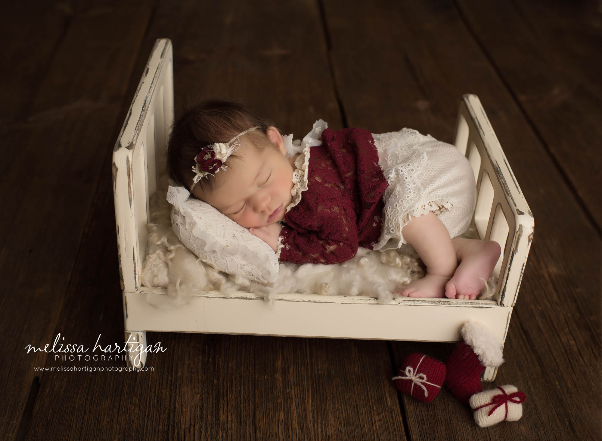 newborn baby girl posed on wooden newborn prop bed wearing red baby girl outfit for chirstmas newborn photography holiday set up