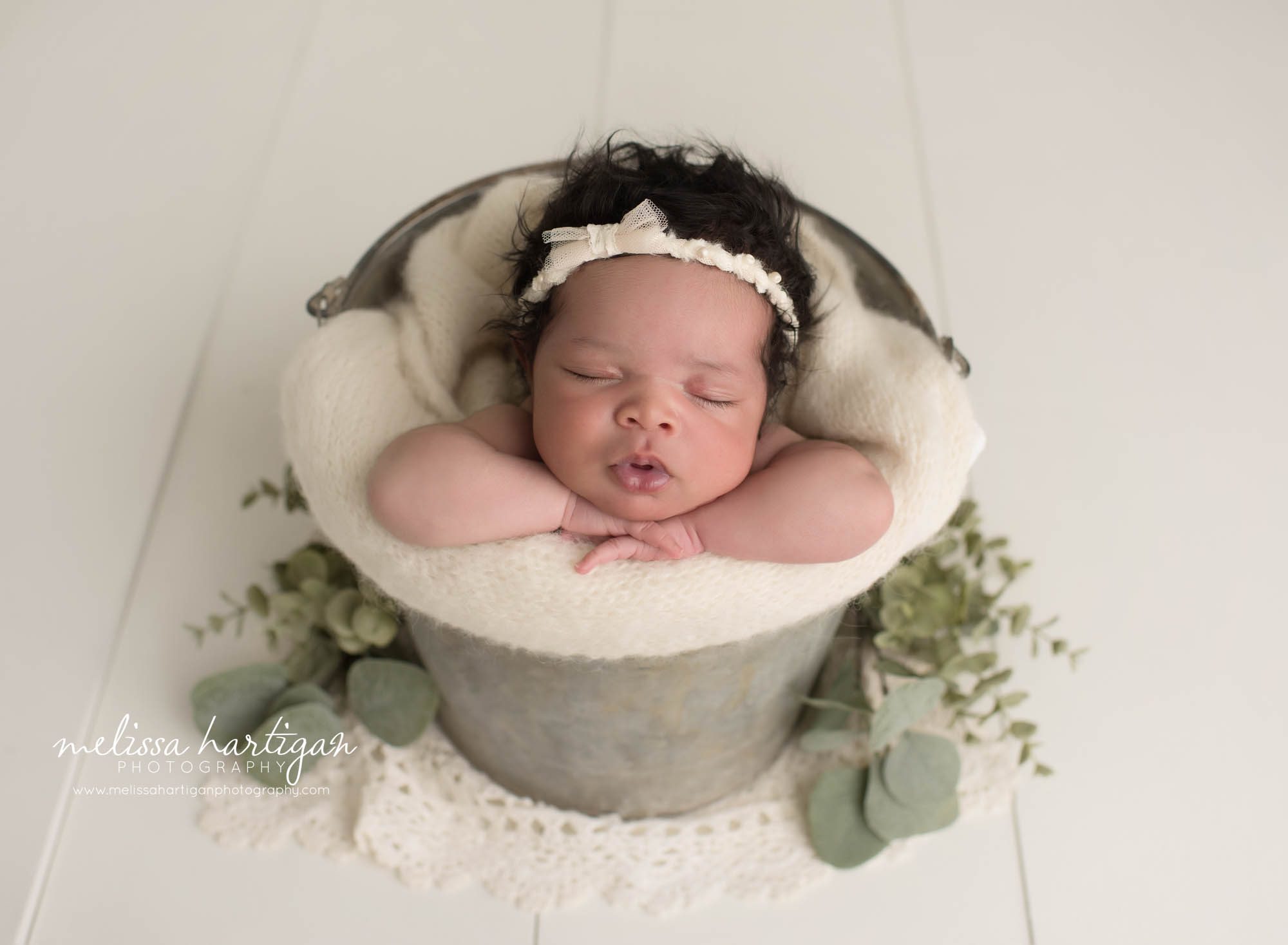 newborn baby girl posed in bucket wearing cream headband newborn photography manchester