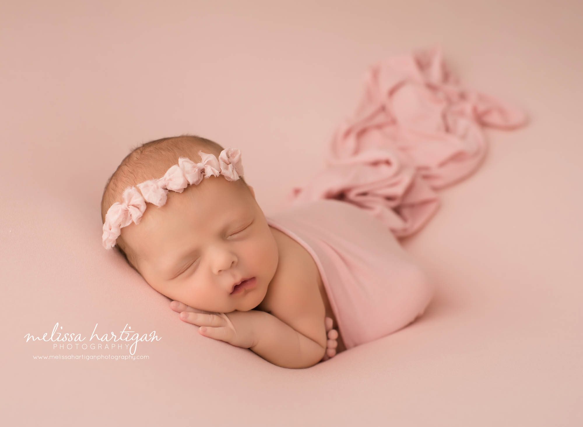 newborn baby girl posed on pink backdrop draped with pink wrap wearing pink bow headband farmington CT baby photography