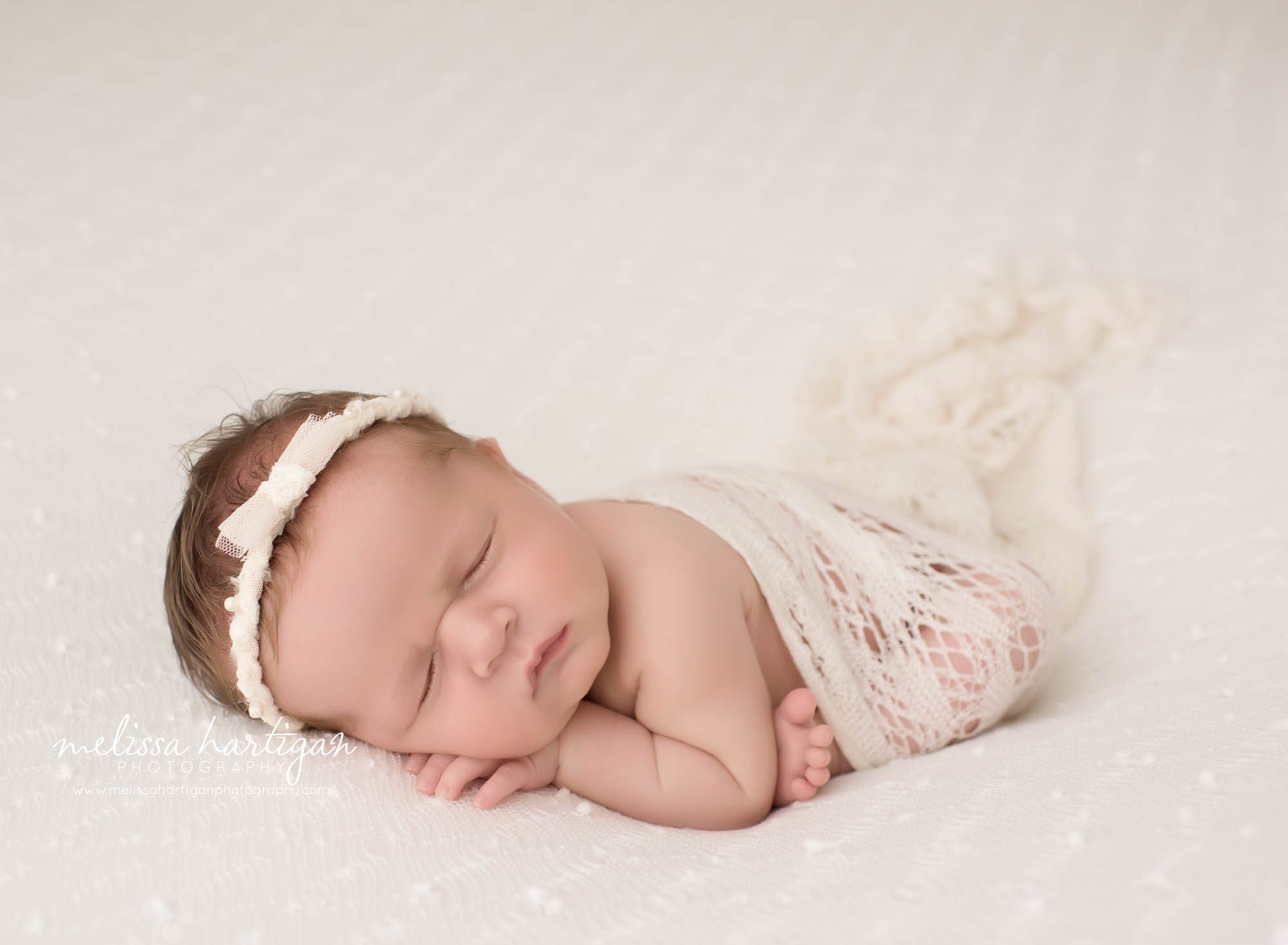 newborn baby girl posed on tummy wearing headband and knit wrap draped over her back