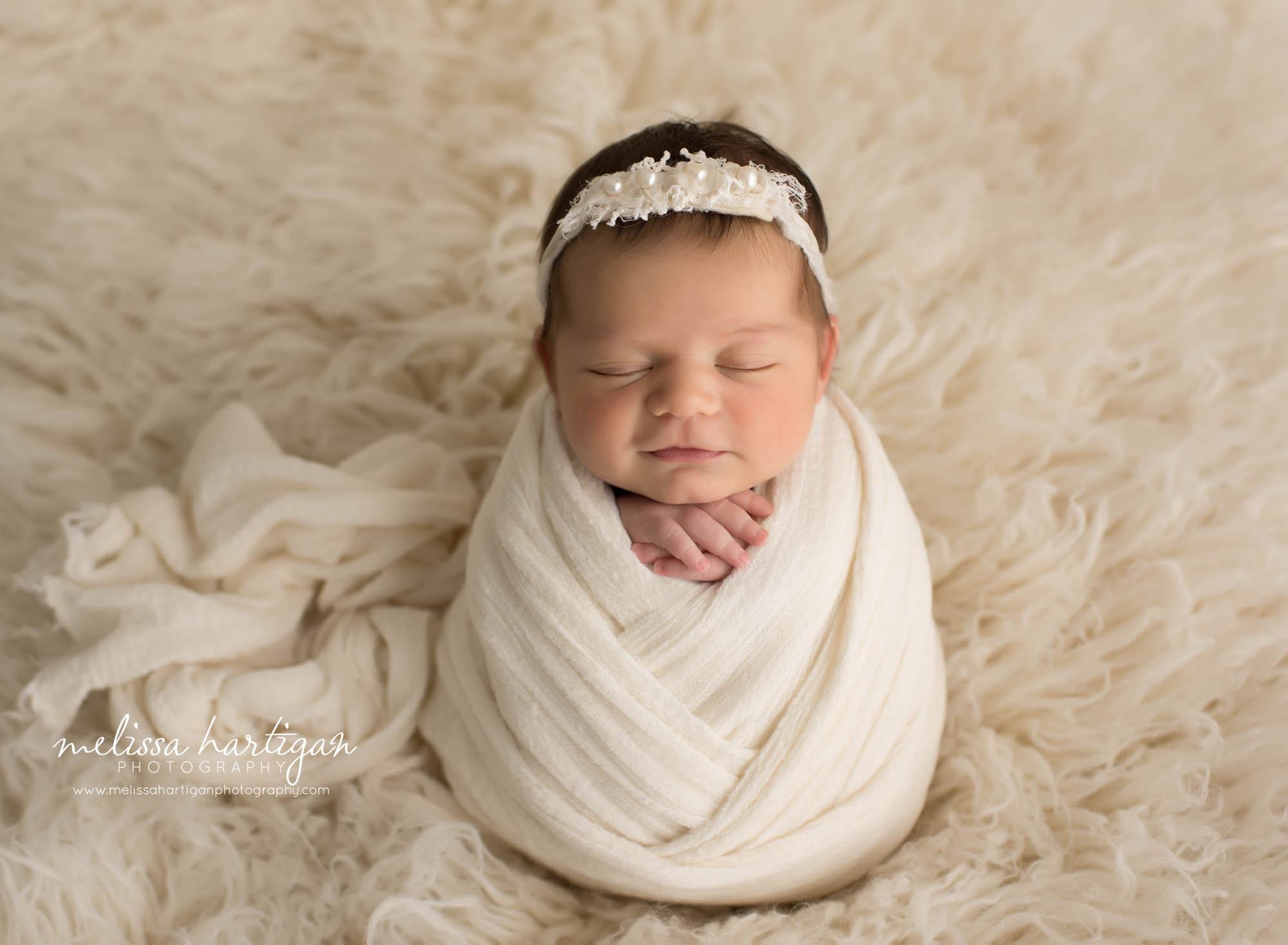 newborn baby girl posed in white wrap on white cream flokati rug 