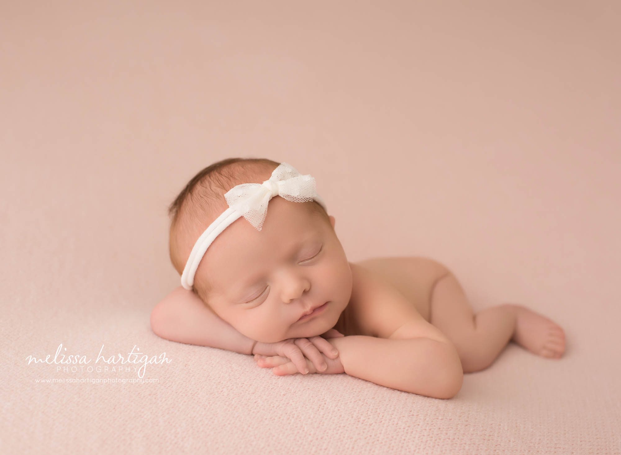newborn baby girl posed on pink backdrop with hands under chin