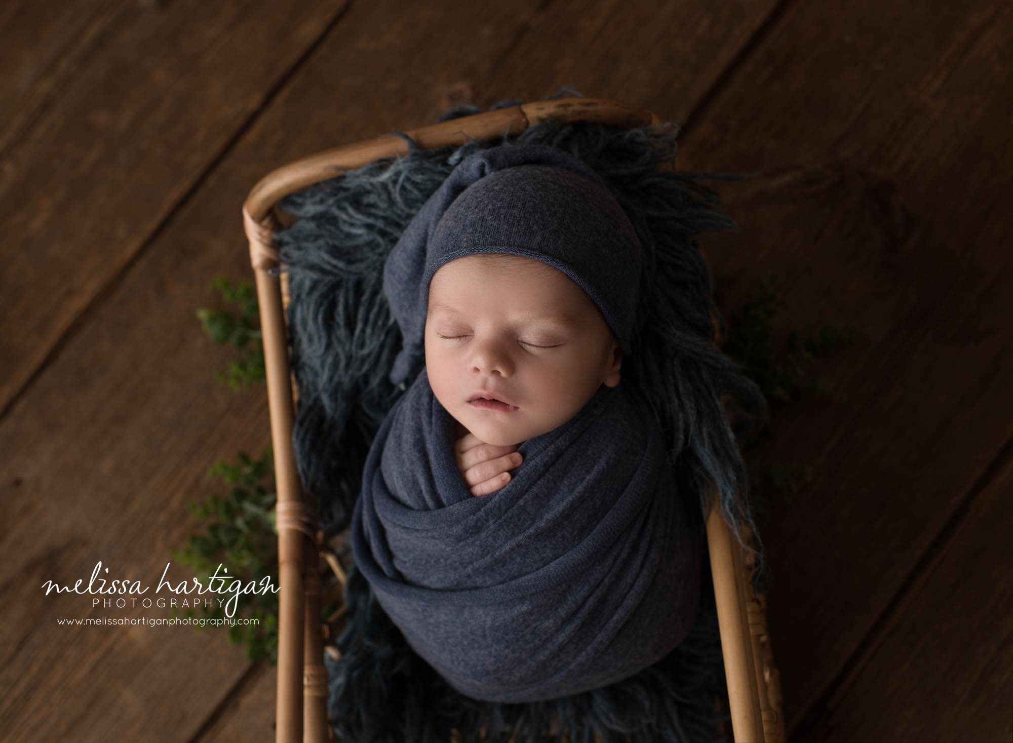 newborn baby boy posed in basket wearing blue sleepy cap and wrapped in blue wrap ct newborn photography