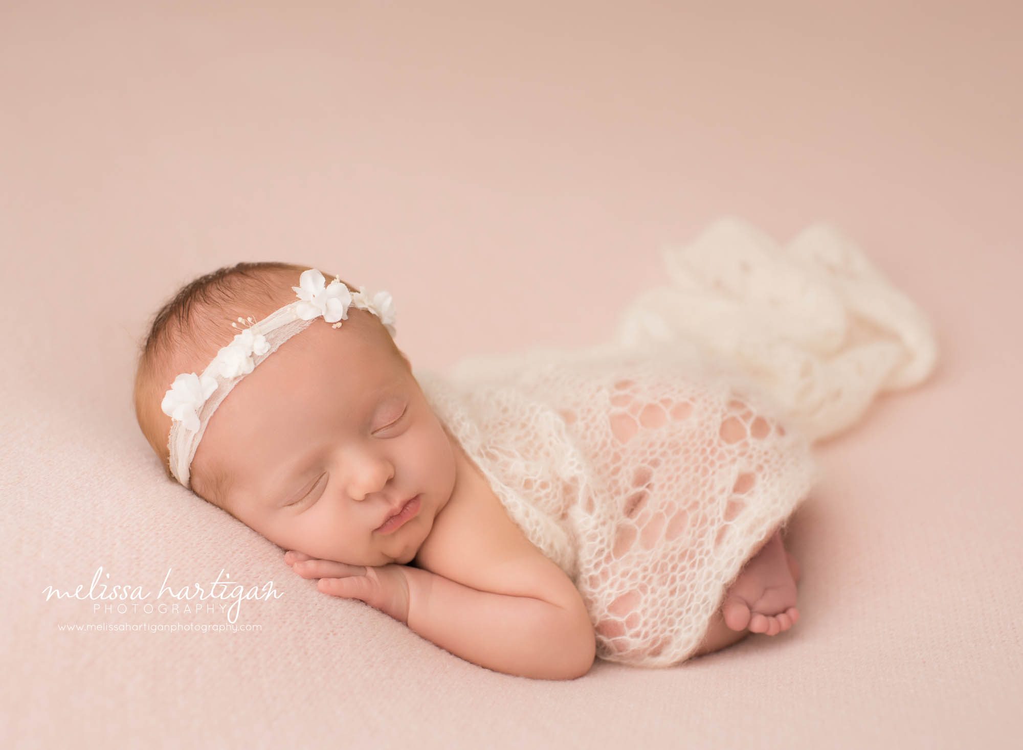 newborn baby girl posed on tummy wearing white flower headband and white knit lace draped over