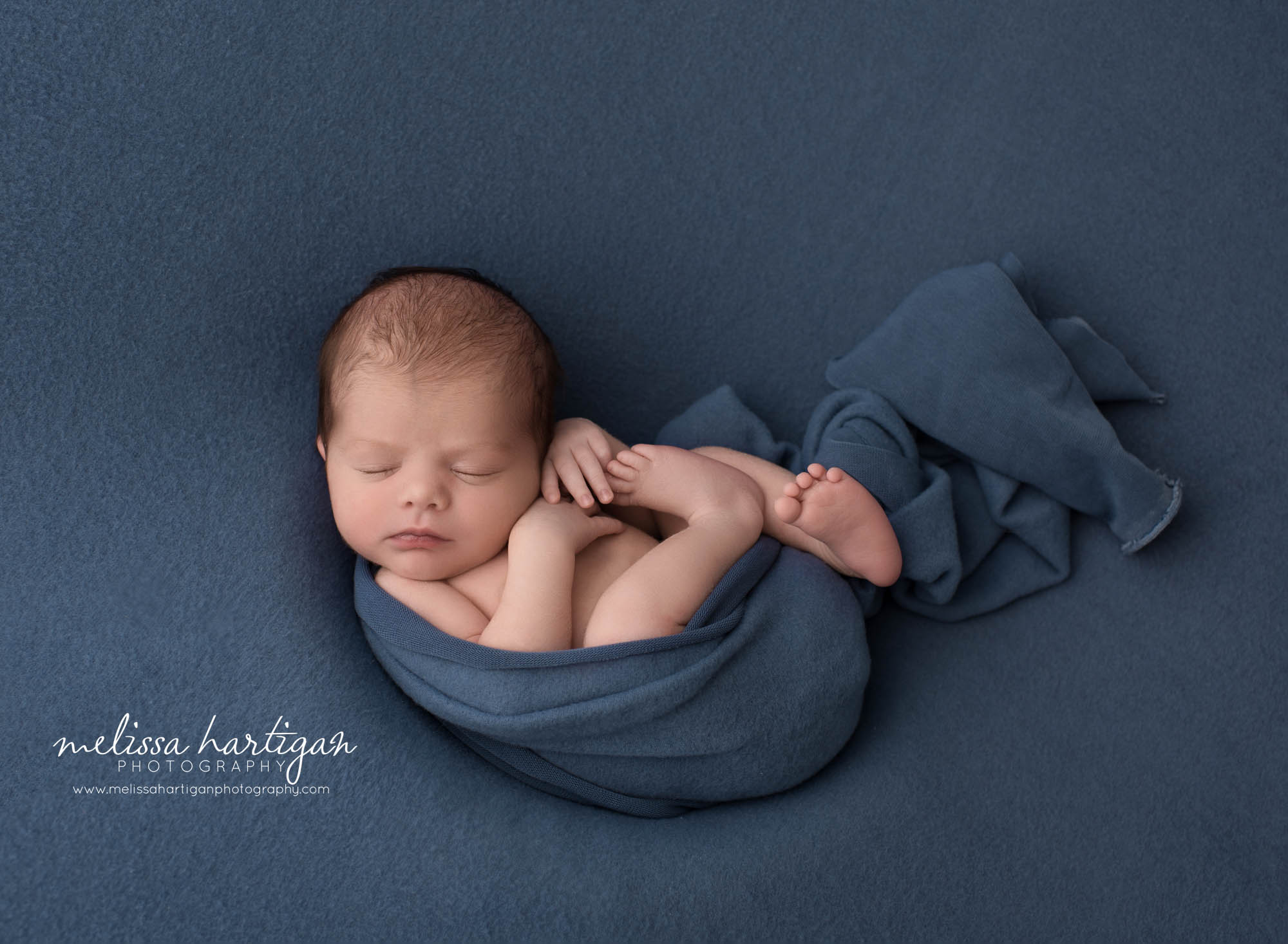 newborn baby boy posed on blue backdrop wrapped in blue wrap newborn photographer scotland ct windham county