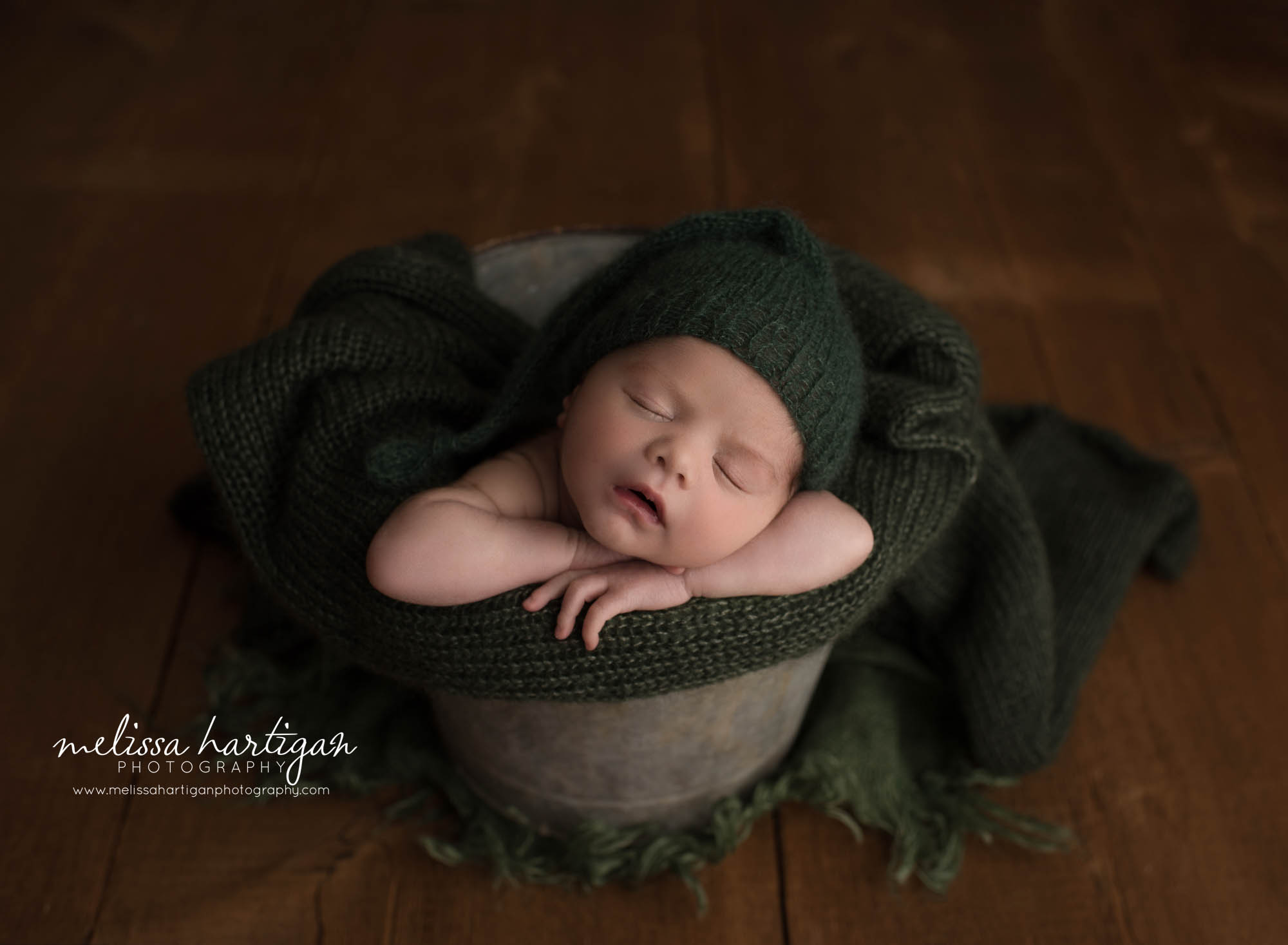 newborn baby boy posed in bucket wearing dark green knitted sleepy cap