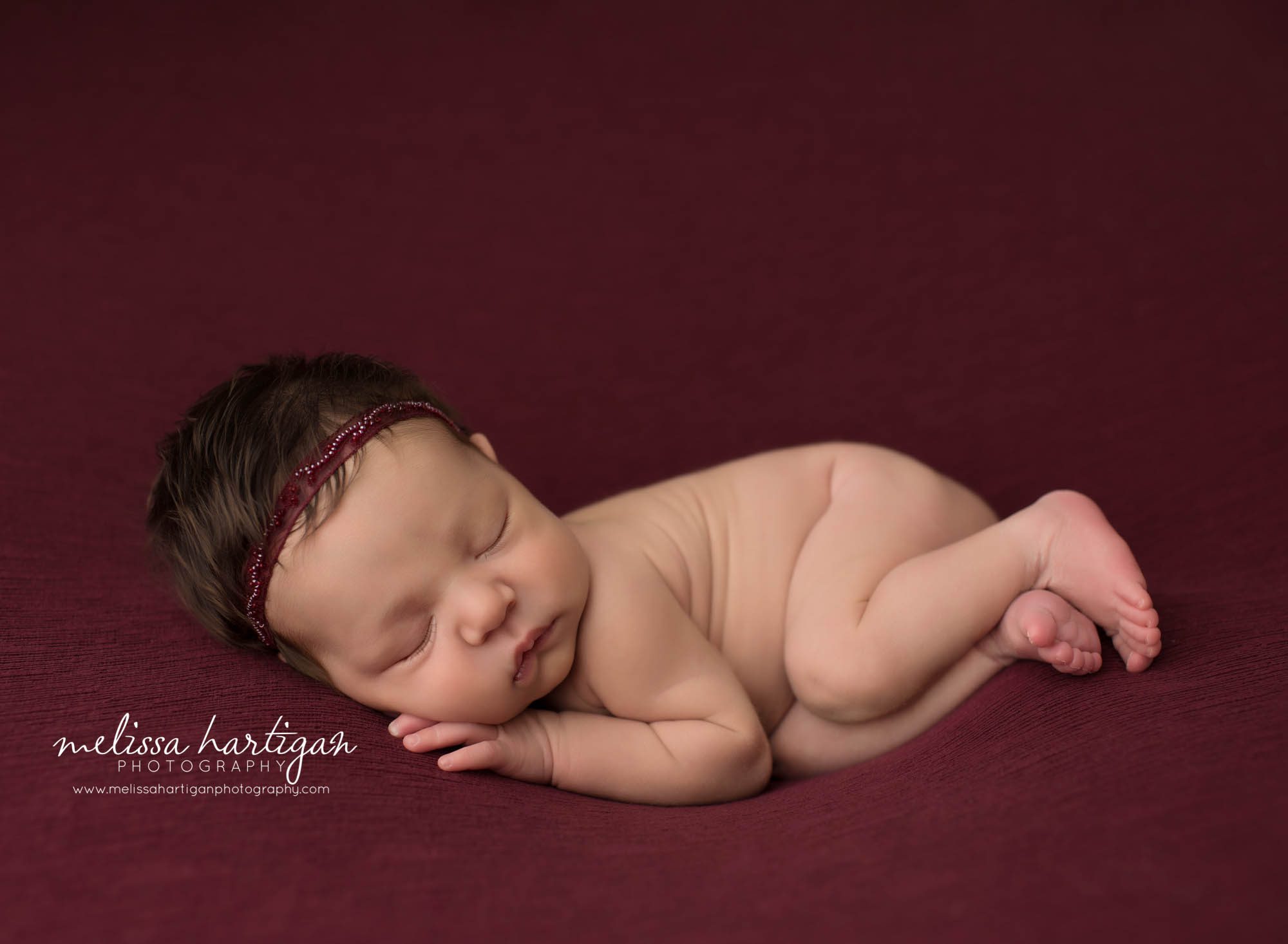 newborn baby girl posed on burgundy backdrop wearing newborn baby girls headband tolldand CT newborn photography
