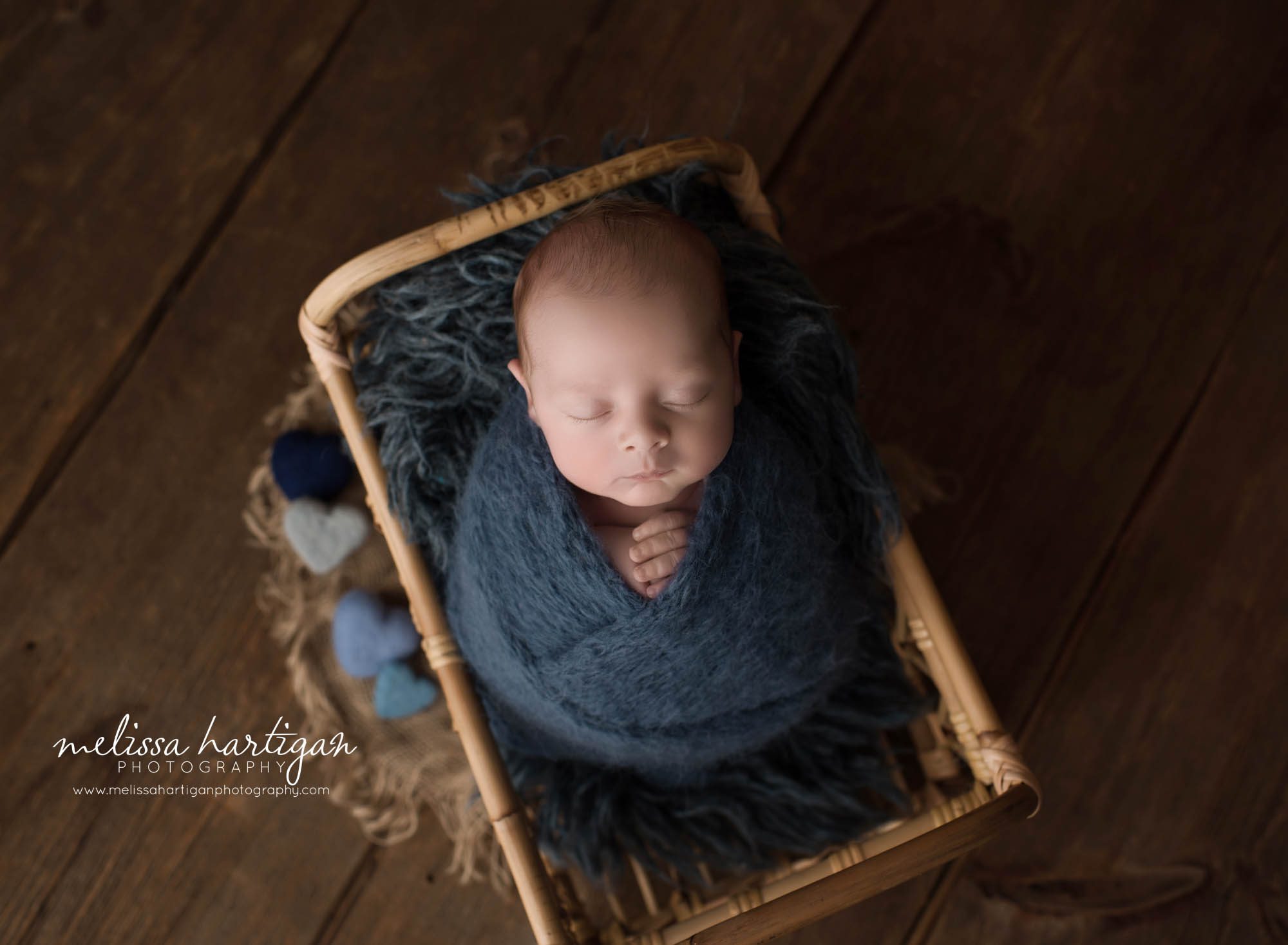 newborn baby boy posed in basket wrapped in knitted navy blue wrap with blue felted hearts