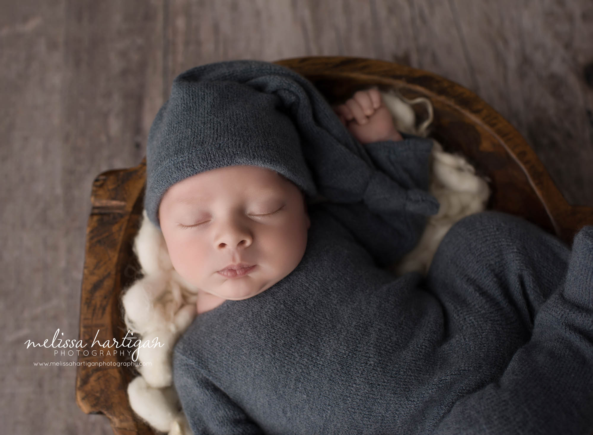 newborn baby boy posed in bowl wearing blue outfit and sleepy cap