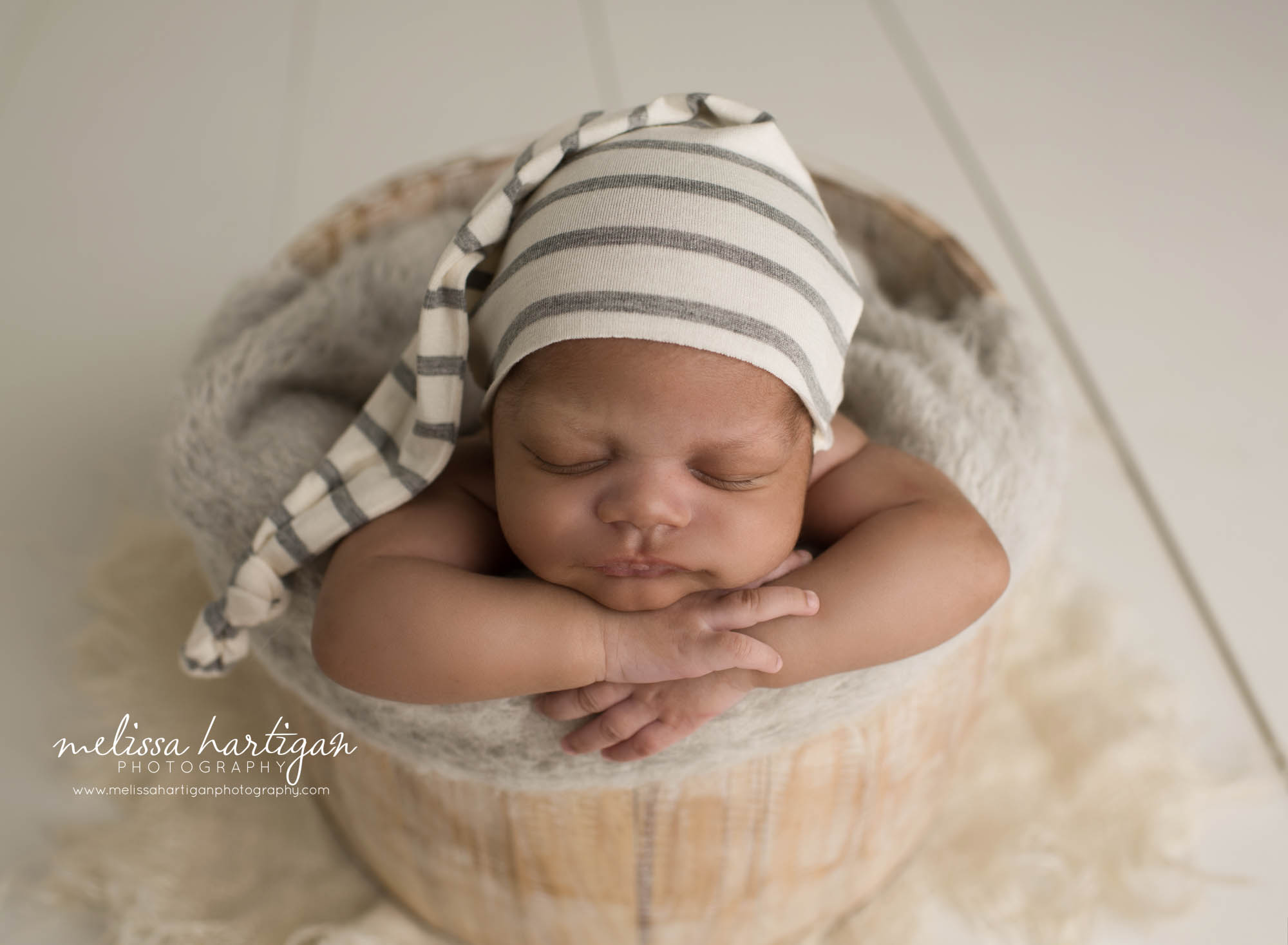 newborn baby boy posed in wooden bucket wearing cream and gray stripped sleepy cap CT Newborn photography