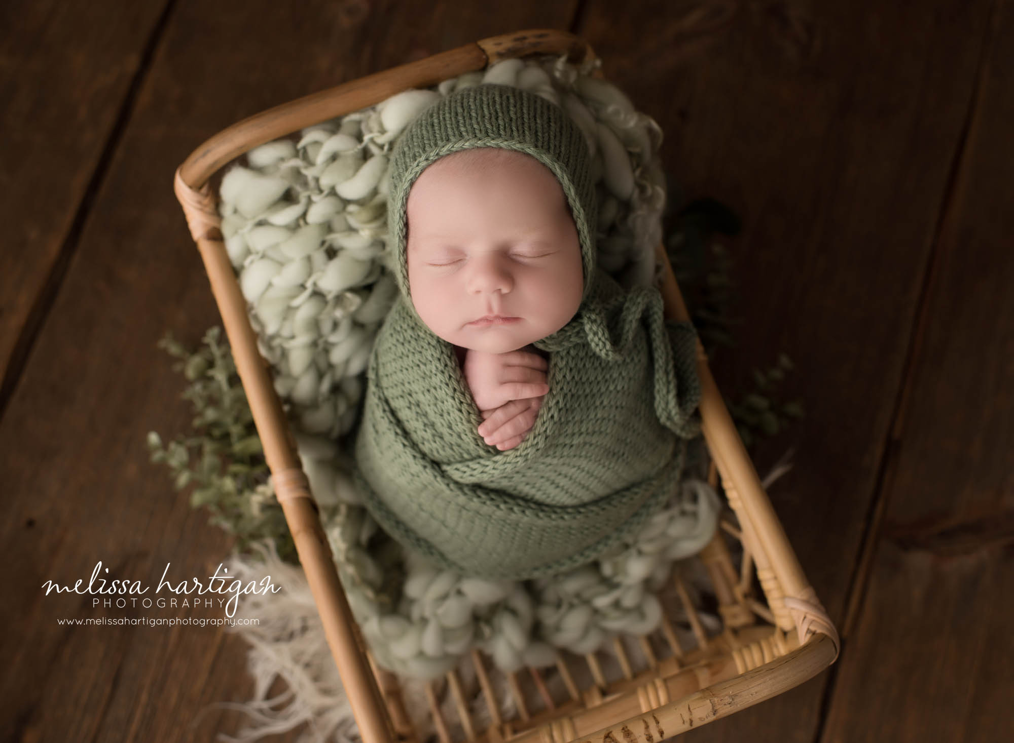 newborn baby girl posed in basket with sage green knitted wrap and matching bonnet