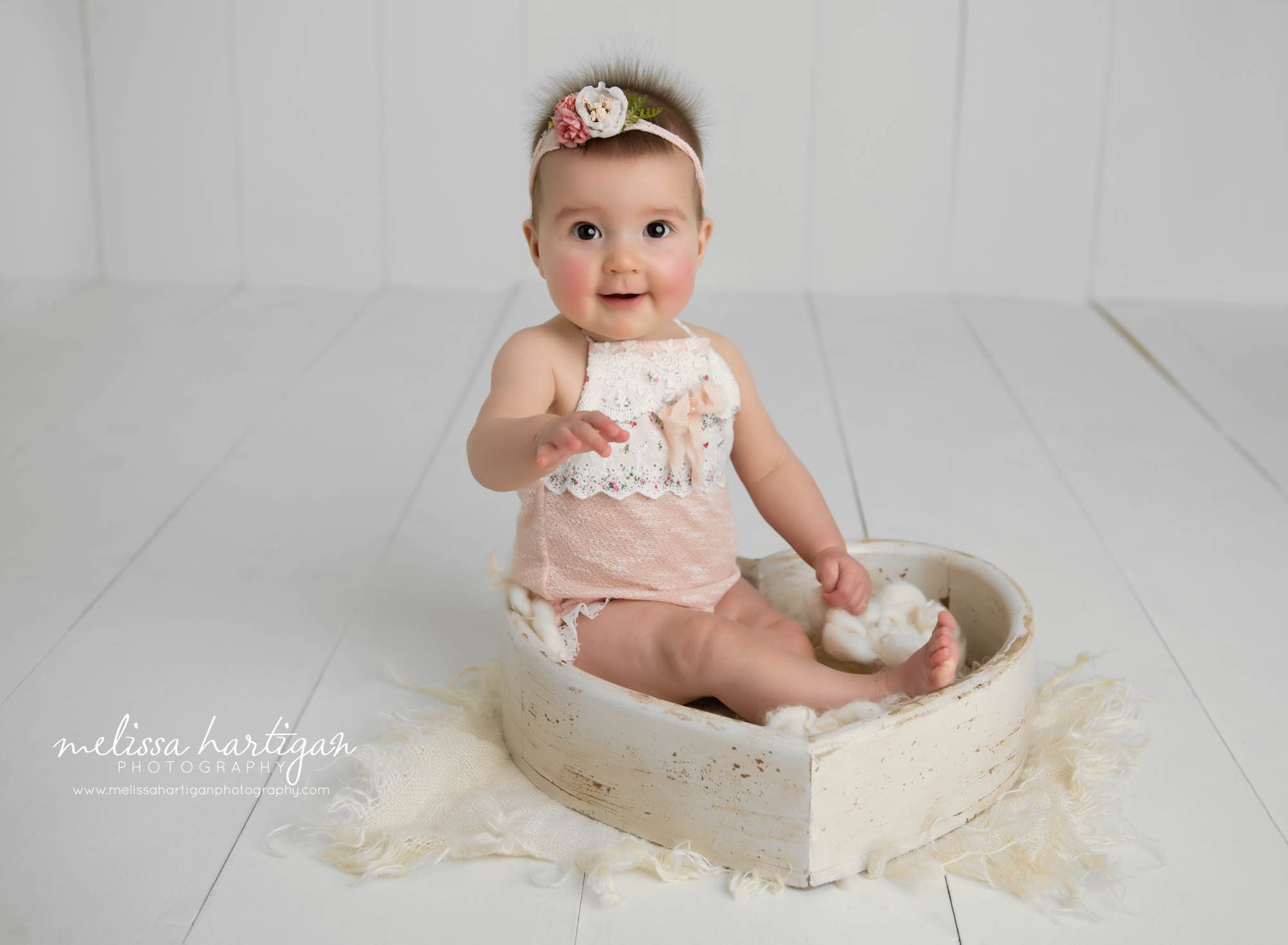 baby girl happy smiling sitting in cream wooden heart prop wearing pink and cream lace outfit and flower headband Simsbury baby photography CT