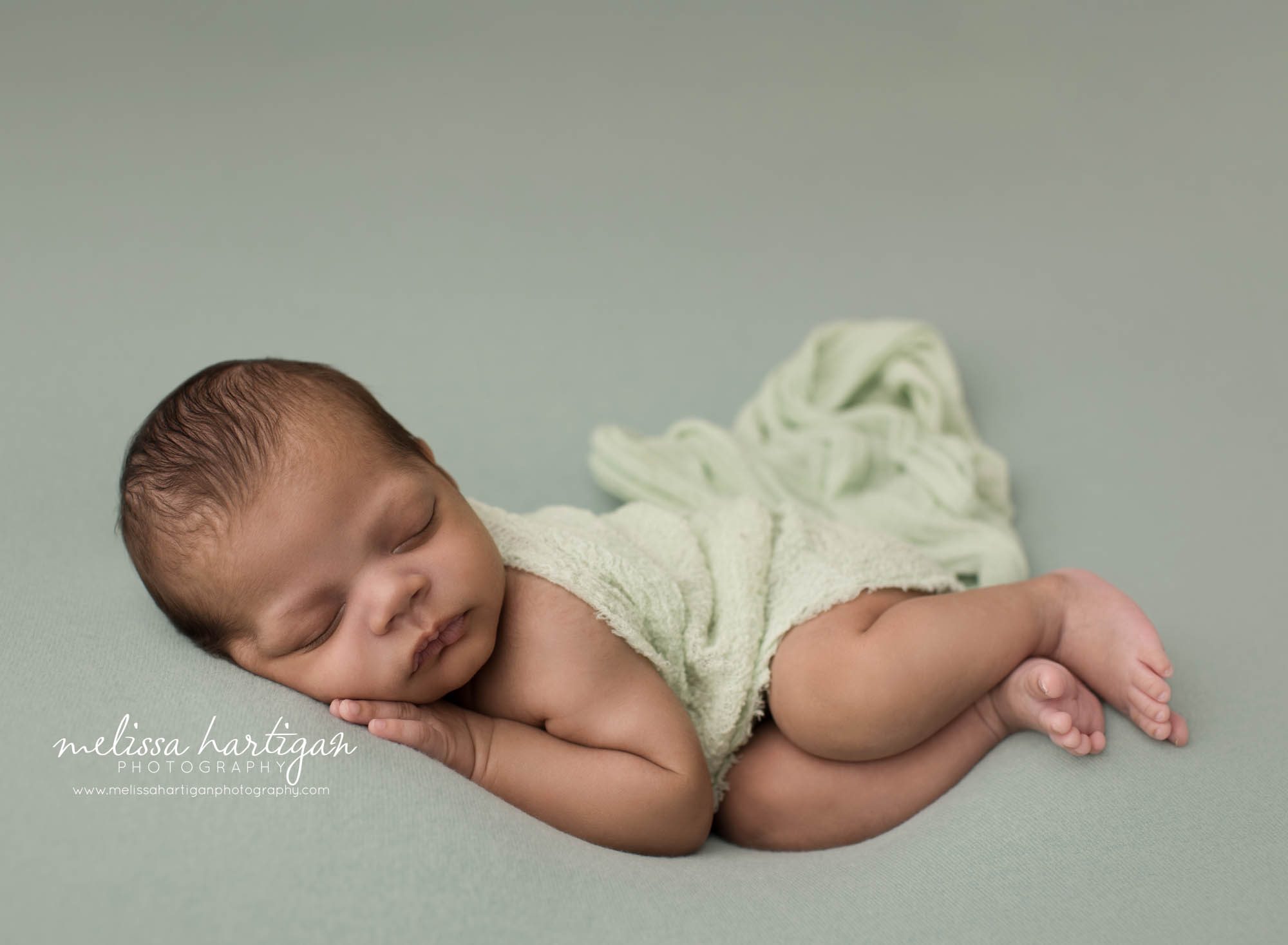 newborn baby boy posed on green backdrop pose don side with green layer wrap draped over him newborn photographer connecticut