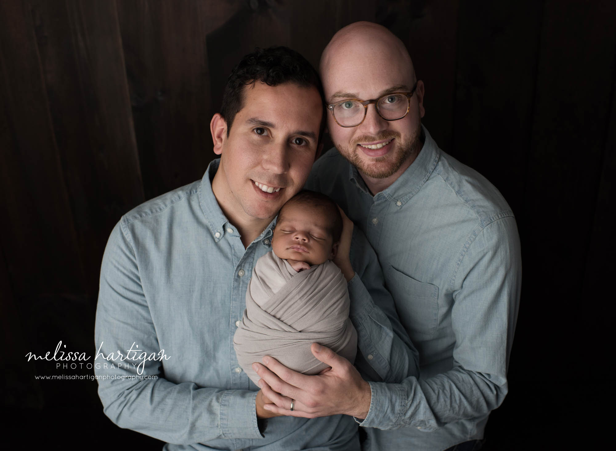 two dads holding newborn son wrapped in gray wrap studio newborn photography CT