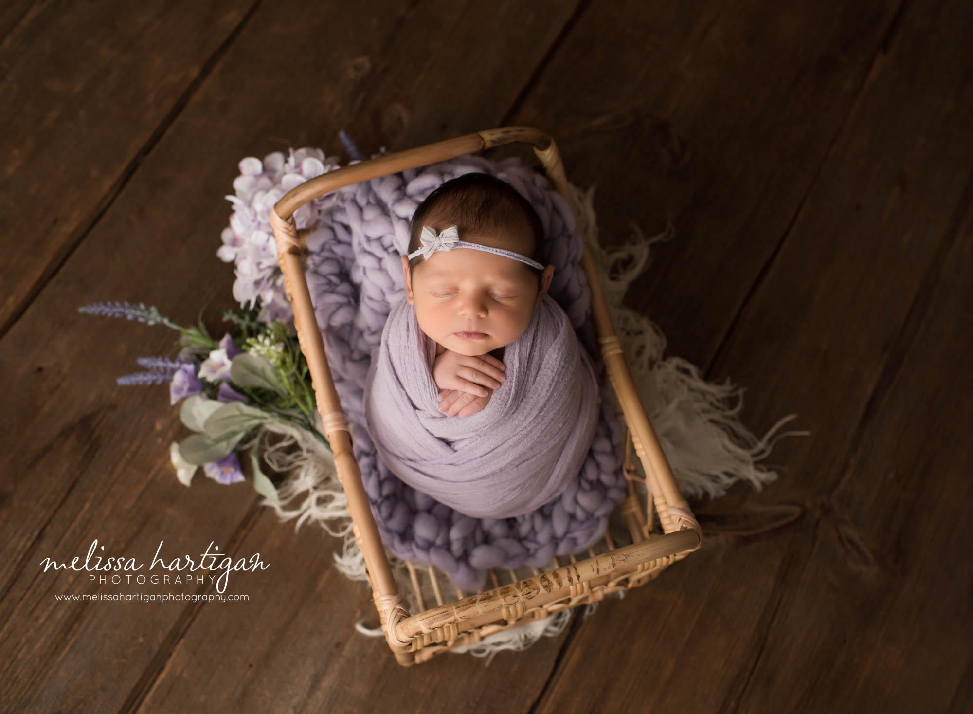 newborn baby girl wrapped in lavendar purple wrap posed in basket with purple flowers Connecticut newborn photographer
