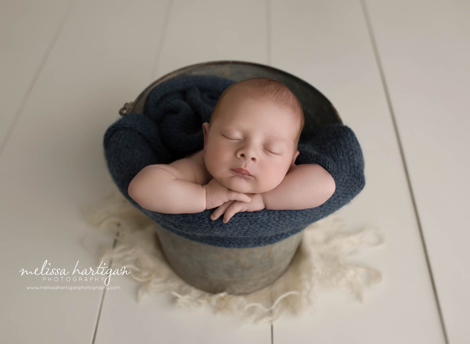 newborn baby boy posed in bucket with navy blue wrap