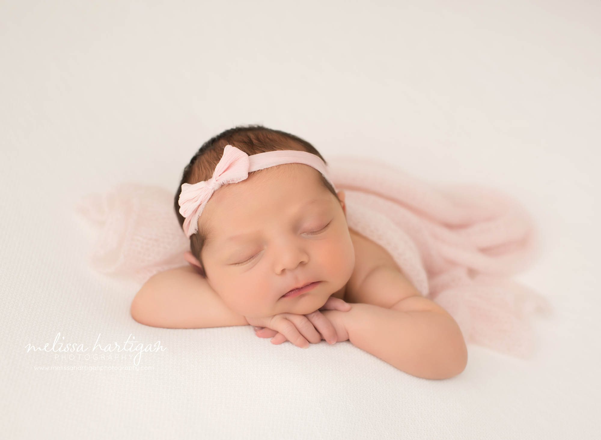 newborn baby girl posed on tummy wearing pink bow headband