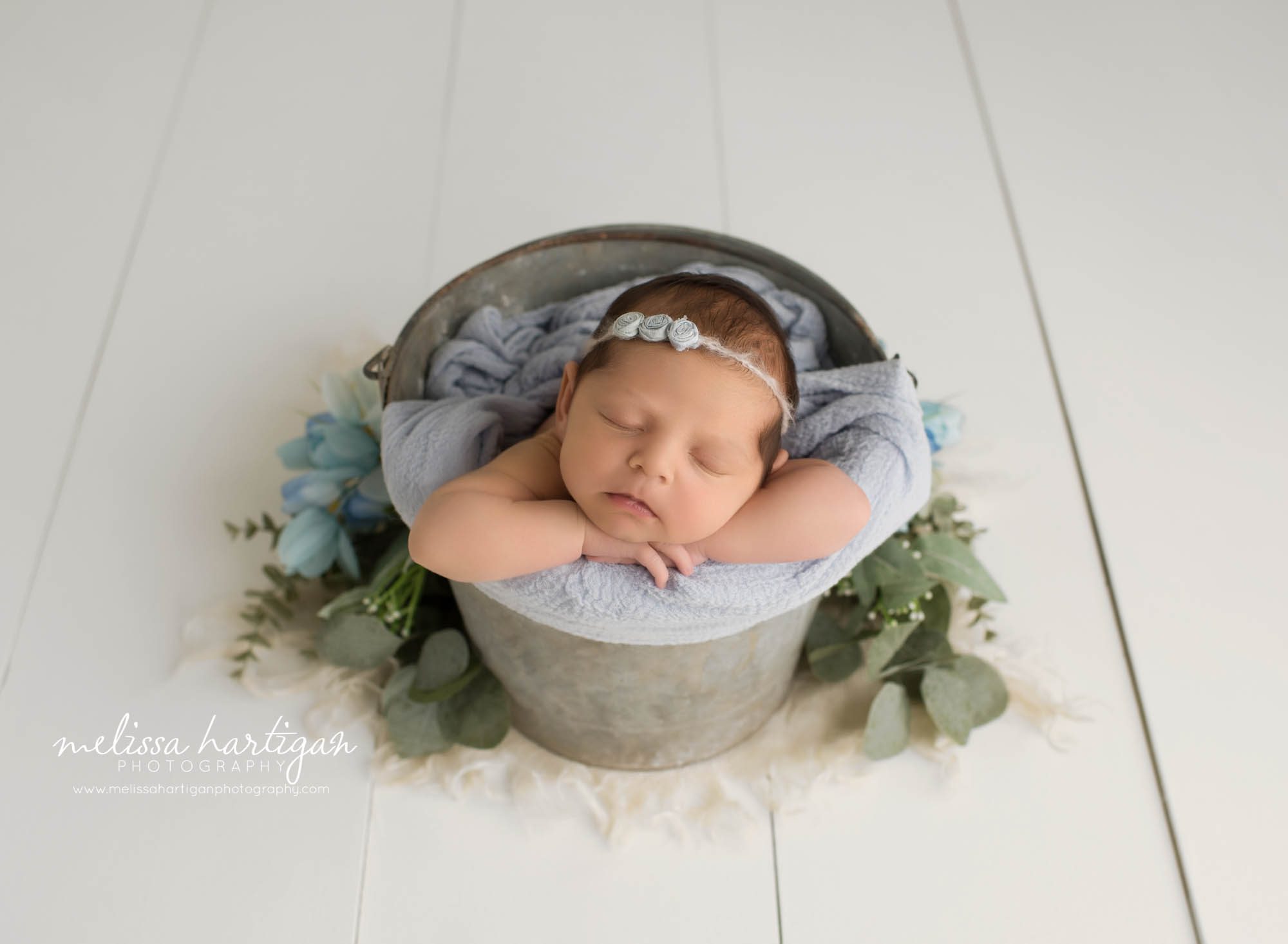 newborn baby girl posed in metal bucket draped with blue layer and blue floral elements newborn photographer NY
