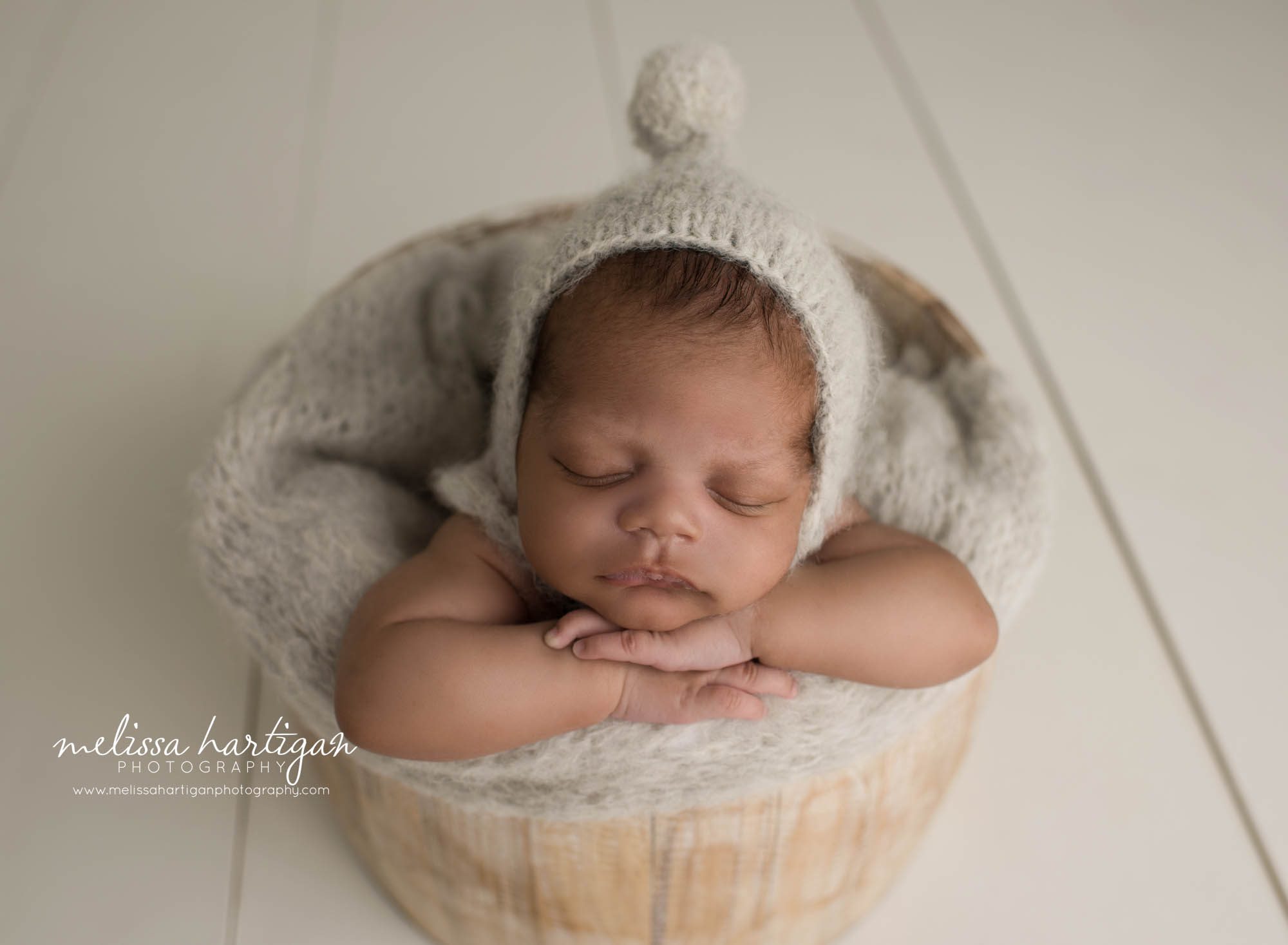 newborn baby boy posed in wooden buckte wearing gray pom knitted bonnet newborn photographer CT
