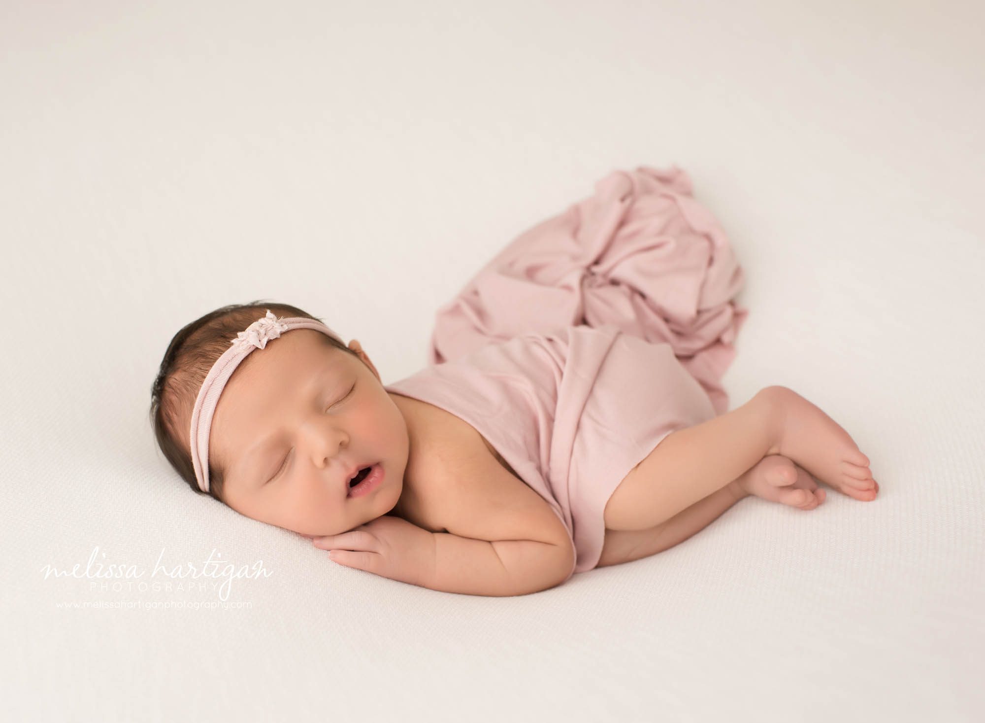 newborn baby girl posed on side with pink layer draped over tummy sleeping wearing headband