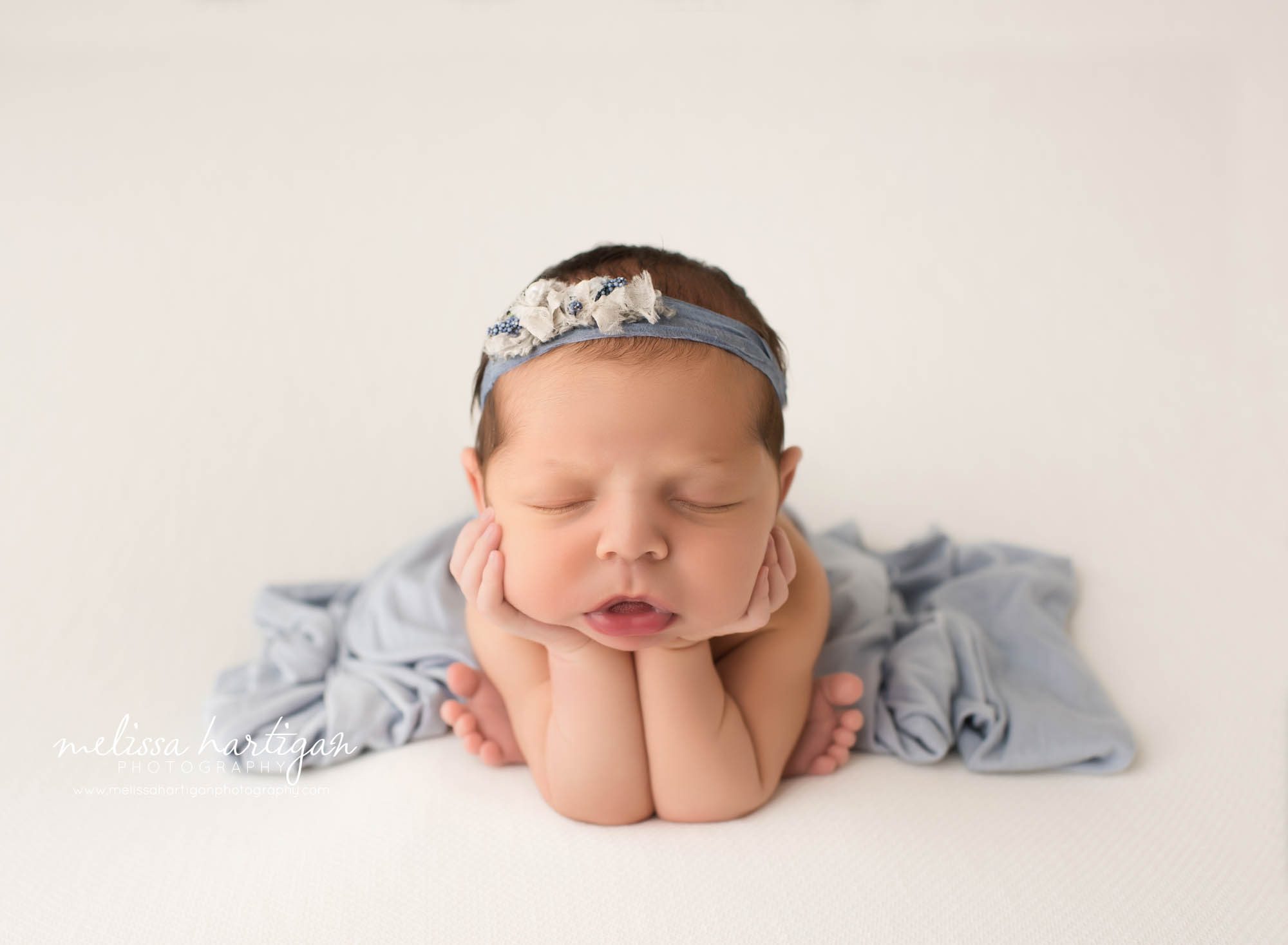 newborn baby girl posed froggy pose on white backdrop with blue drape layer NY newborn photography new York