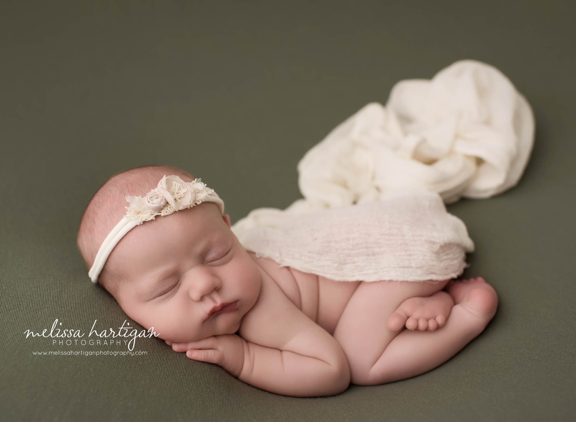 newborn baby girl posed on tummy with hand under cheek wearing cream headband tolland county CT newborn baby photography