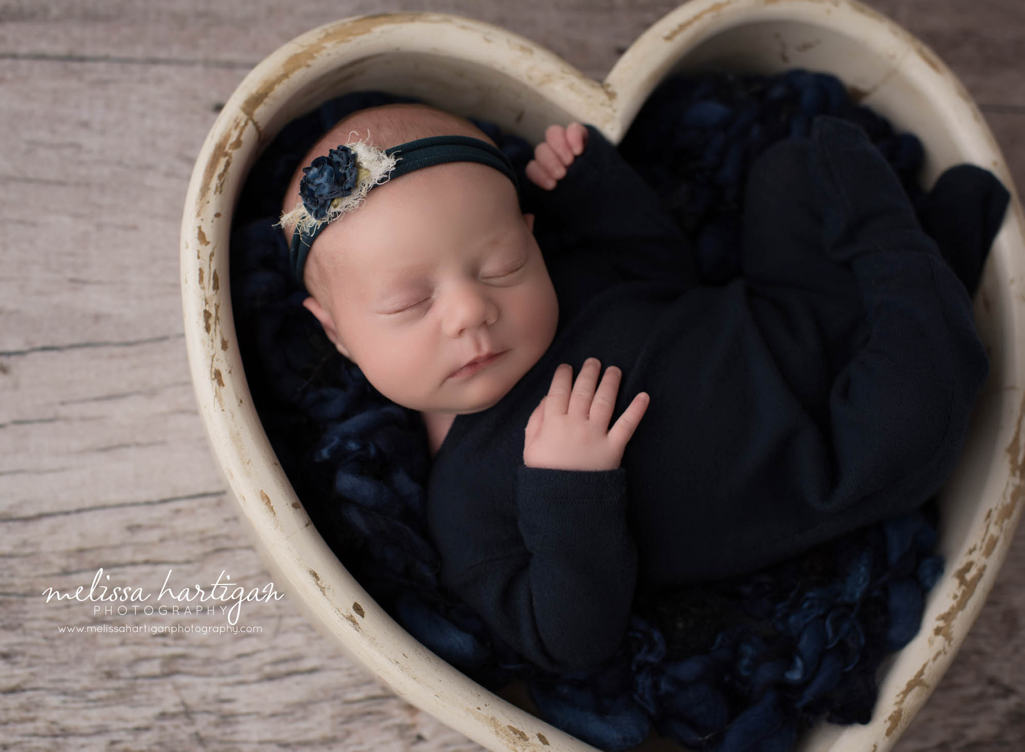 newborn baby girl pose din cream wooden heart prop with navy blue colors