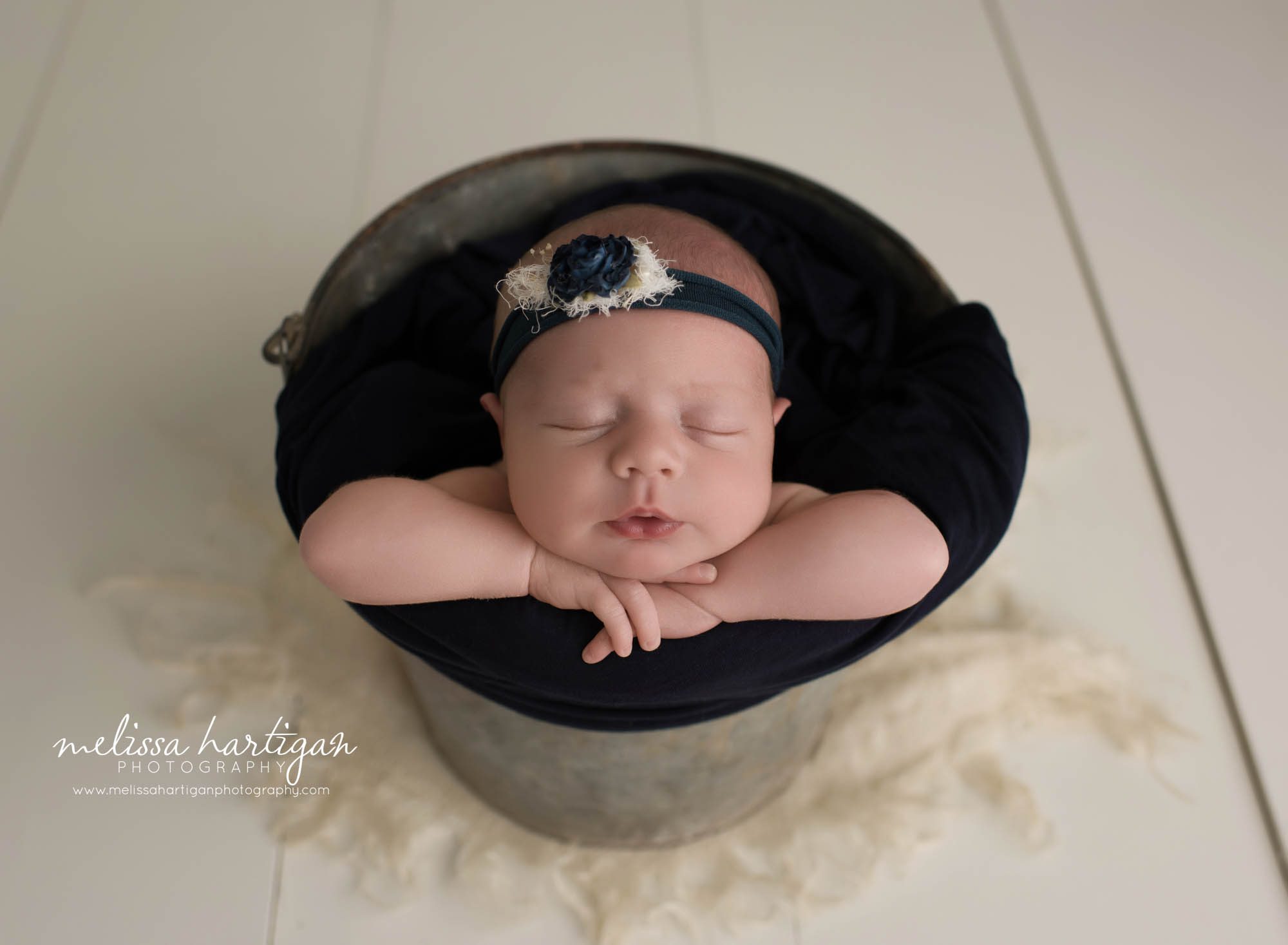 newbonr baby girl posed in metal bucket with navy blue wrap and headband