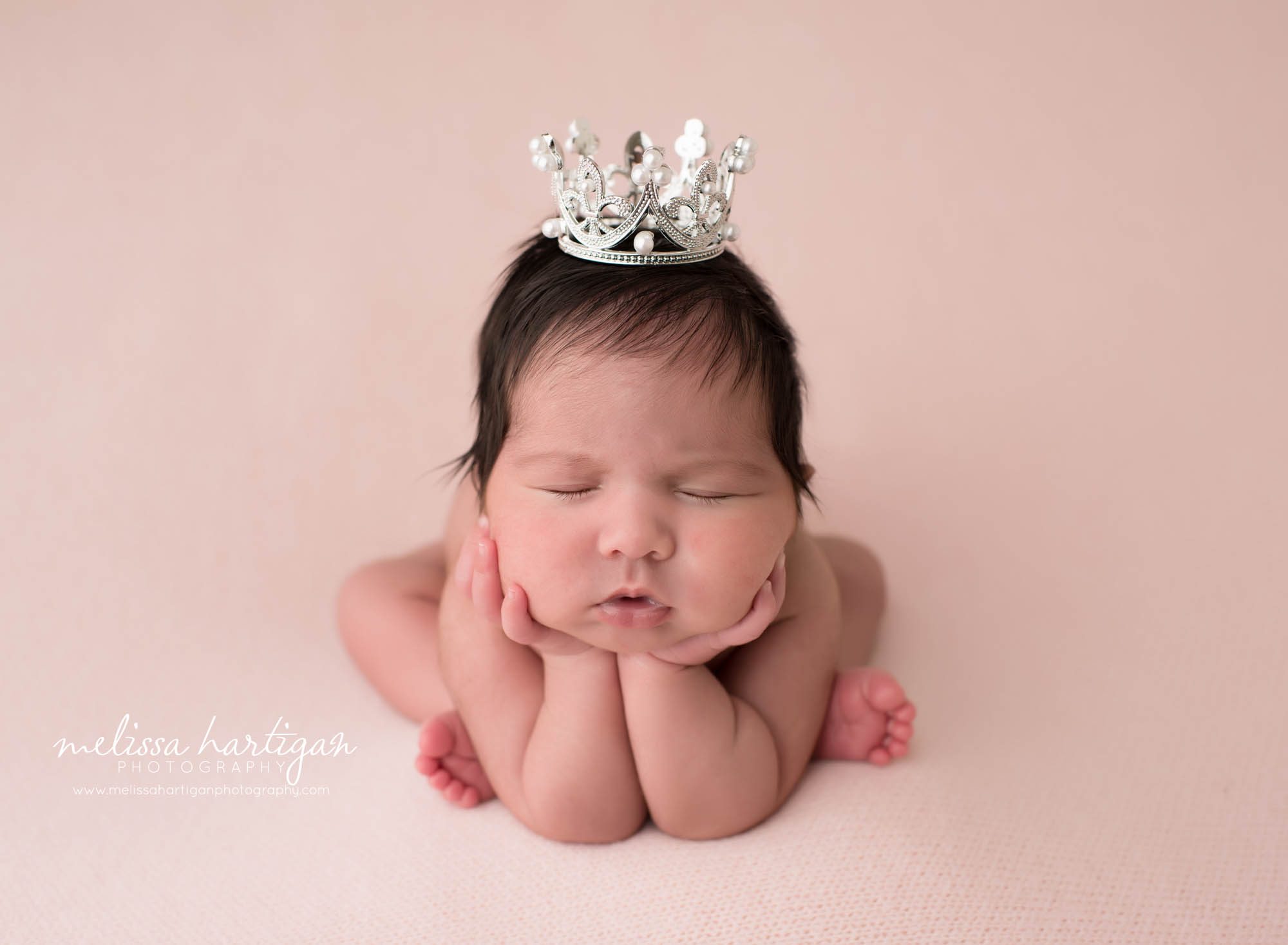newborn baby girl posed on pink backdrop in froggy pose wearing crown