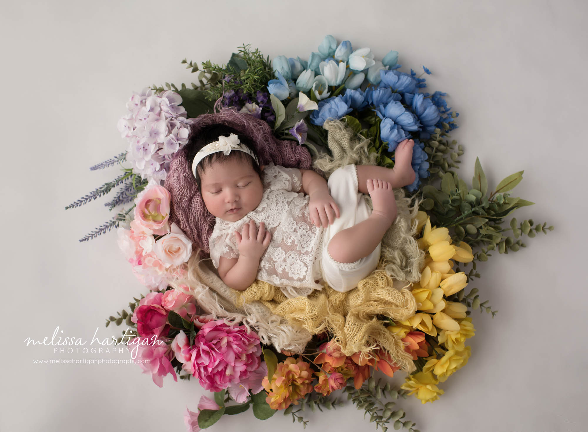 newborn baby girl posed in floral wreath rainbow baby setup