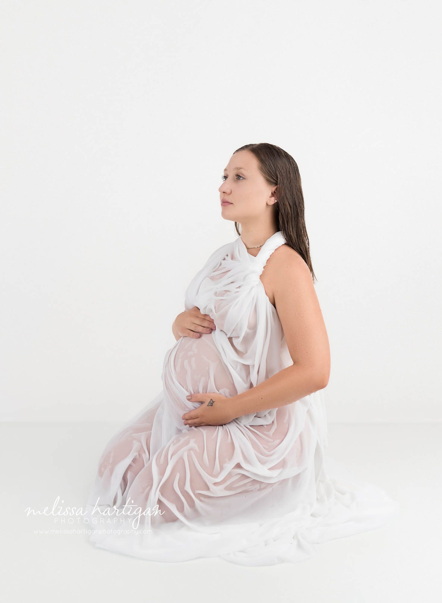 pregnant mom sitting on floor wearing white grecian style maternity dress wet water soaked
