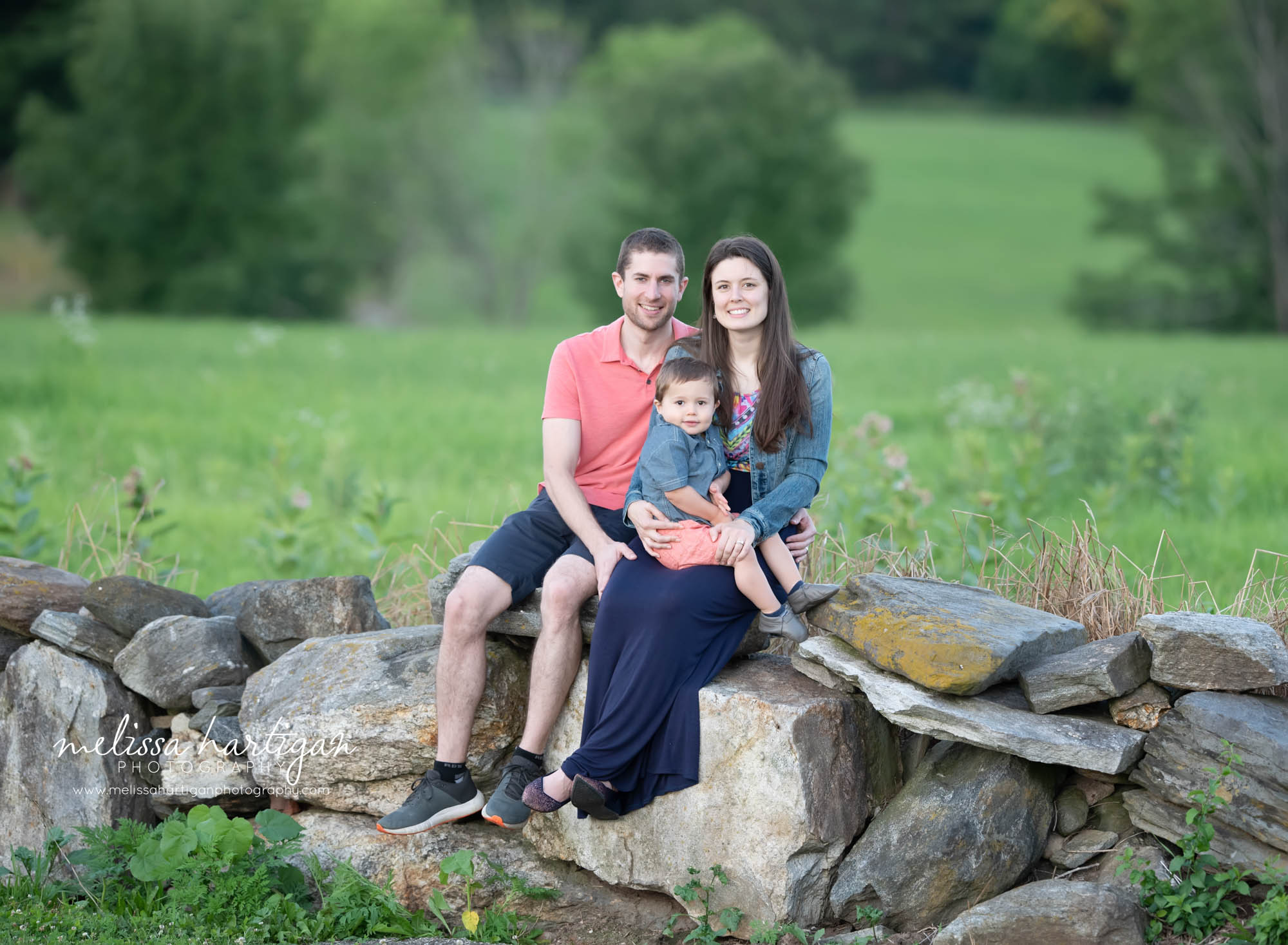 mom dad and little boy sitting all together on rocks family photographer CT