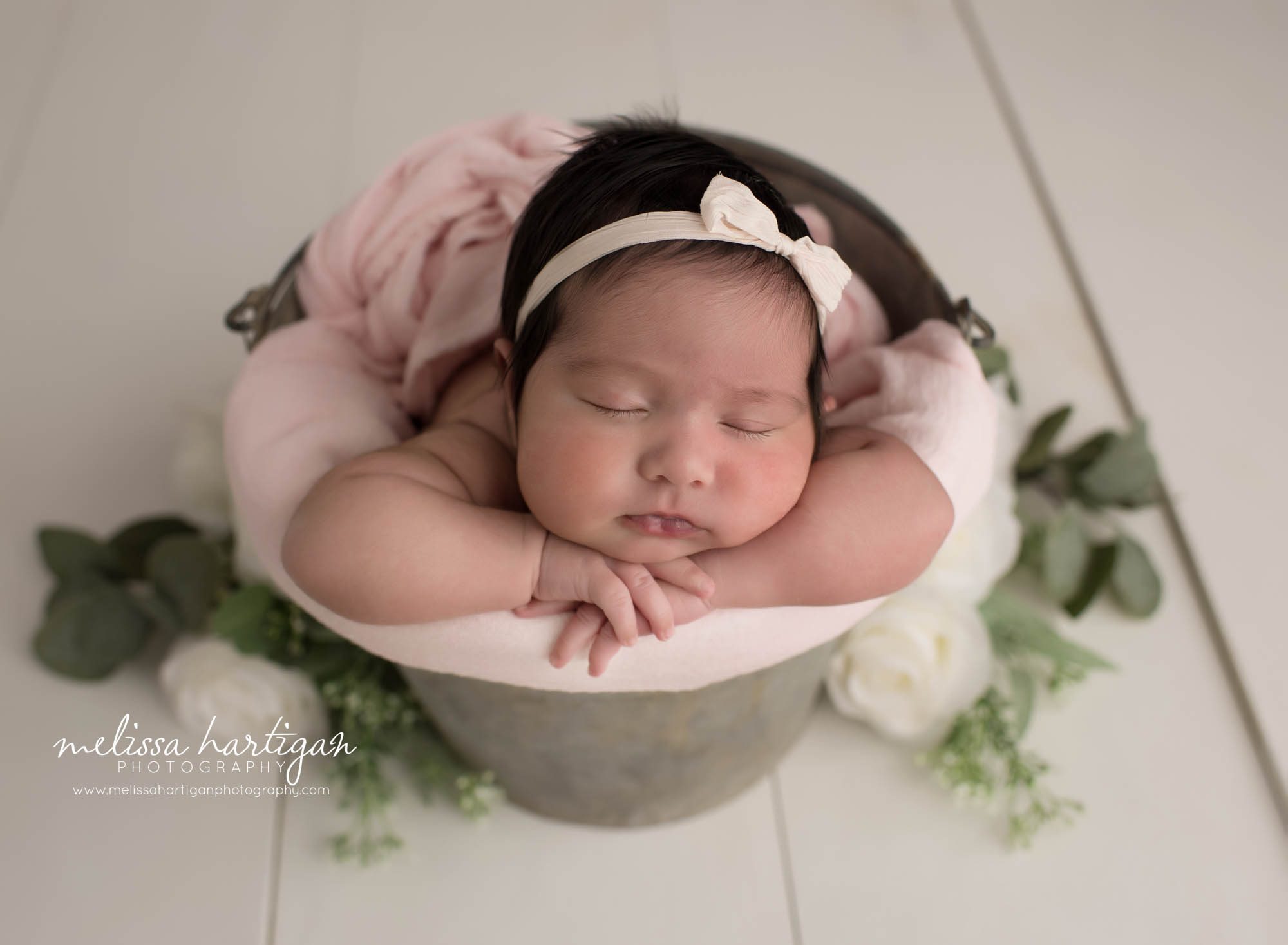 newborn baby girl posed in bucket with pink wrap and green foilage branford ct baby photography