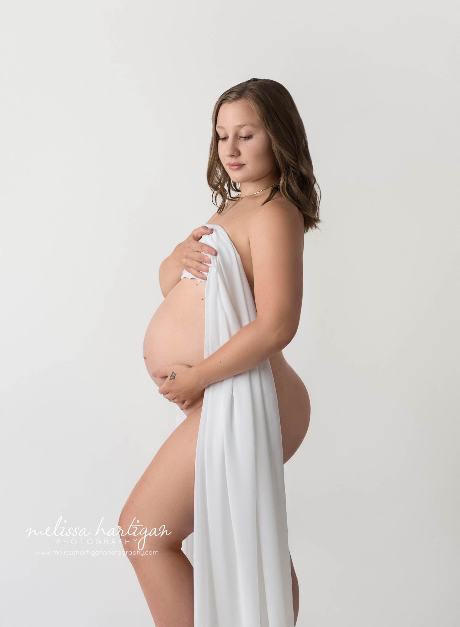 pregnant mom standign studio maternity photography holding draping fabric over baby bump