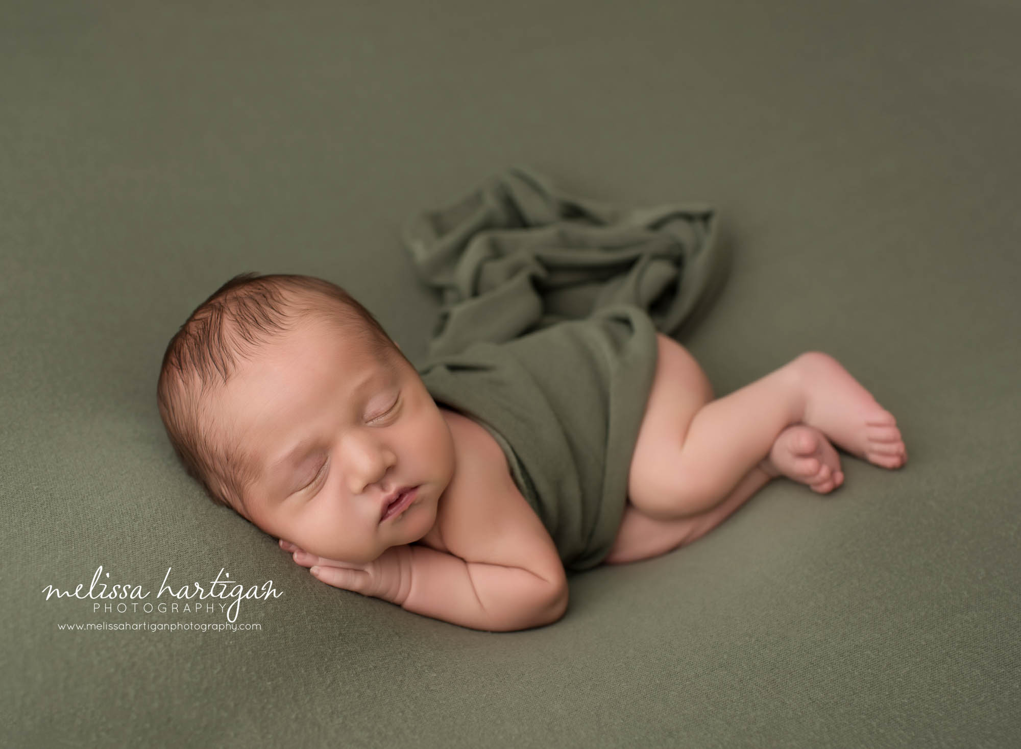 newborn baby boy posed on green backdrop with sage green wrap posed on side sleeping newborn photography griswold CT