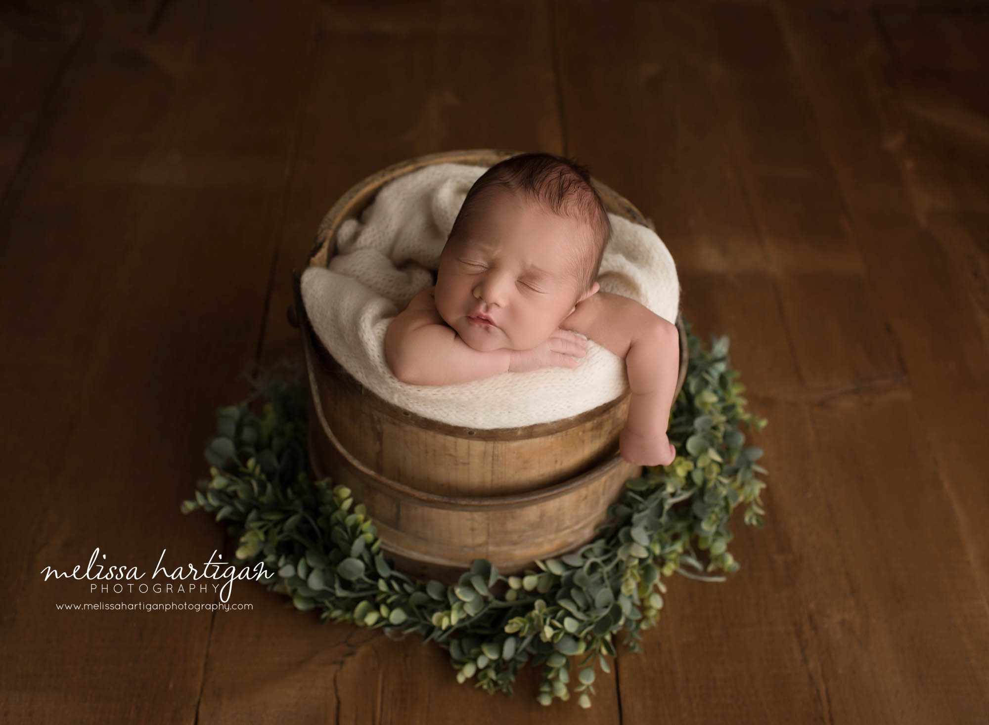 newborn baby boy posed in wooden bucket with green foilage and cream wrap newborn photography griswold CT