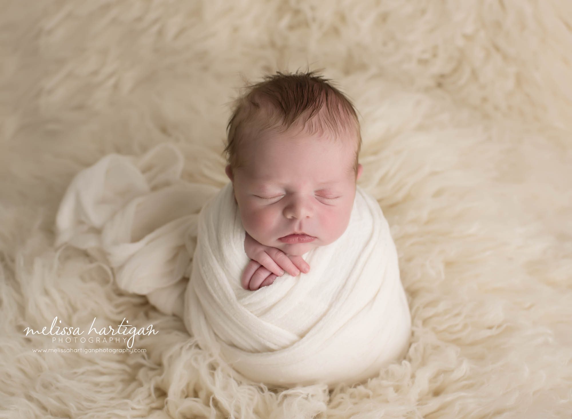 newborn baby boy wrapped in white wrap posed on cream flokati CT newborn and family photographer