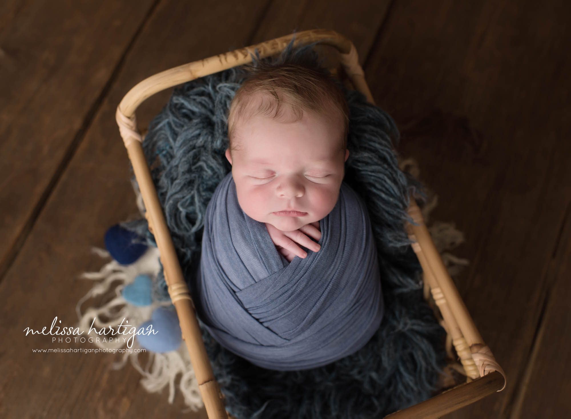 newborn baby boy posed in basket wrapped in blue layer wrap