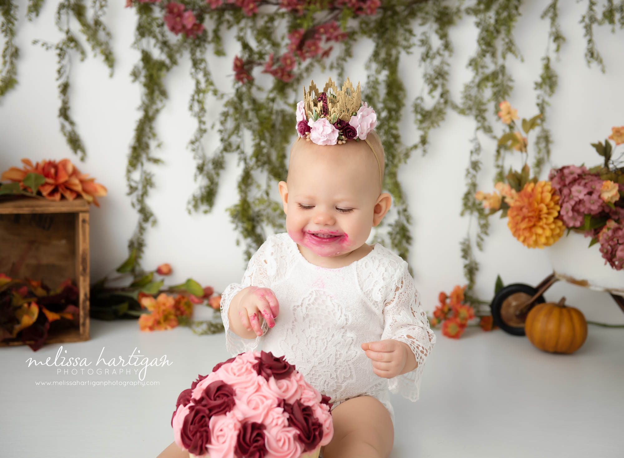happy baby girl digging into cake for first birthday photoshoot