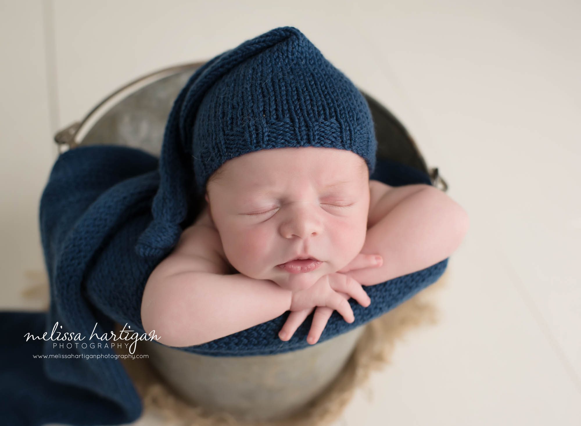 newborn baby boy posed in metal bucket wearing navy blue sleepy cap newborn photography CT