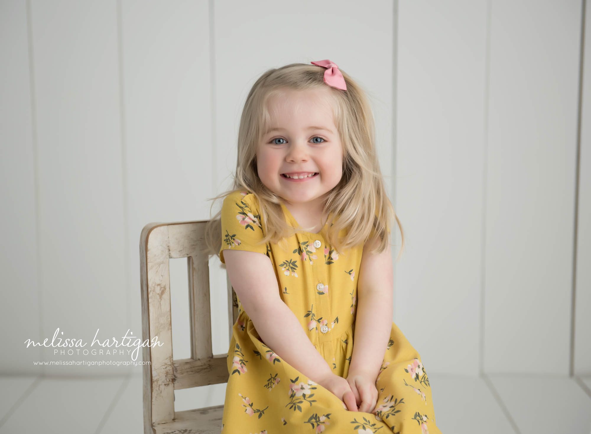 happy smiling little girl posing for photoshoot sitting on wooden chair in studio