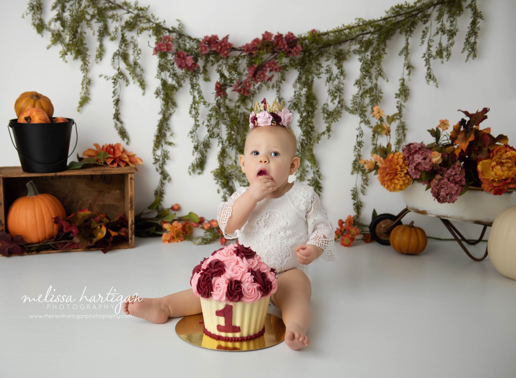 baby girl sitting on floor with 1st birth cake in front of her eating cake