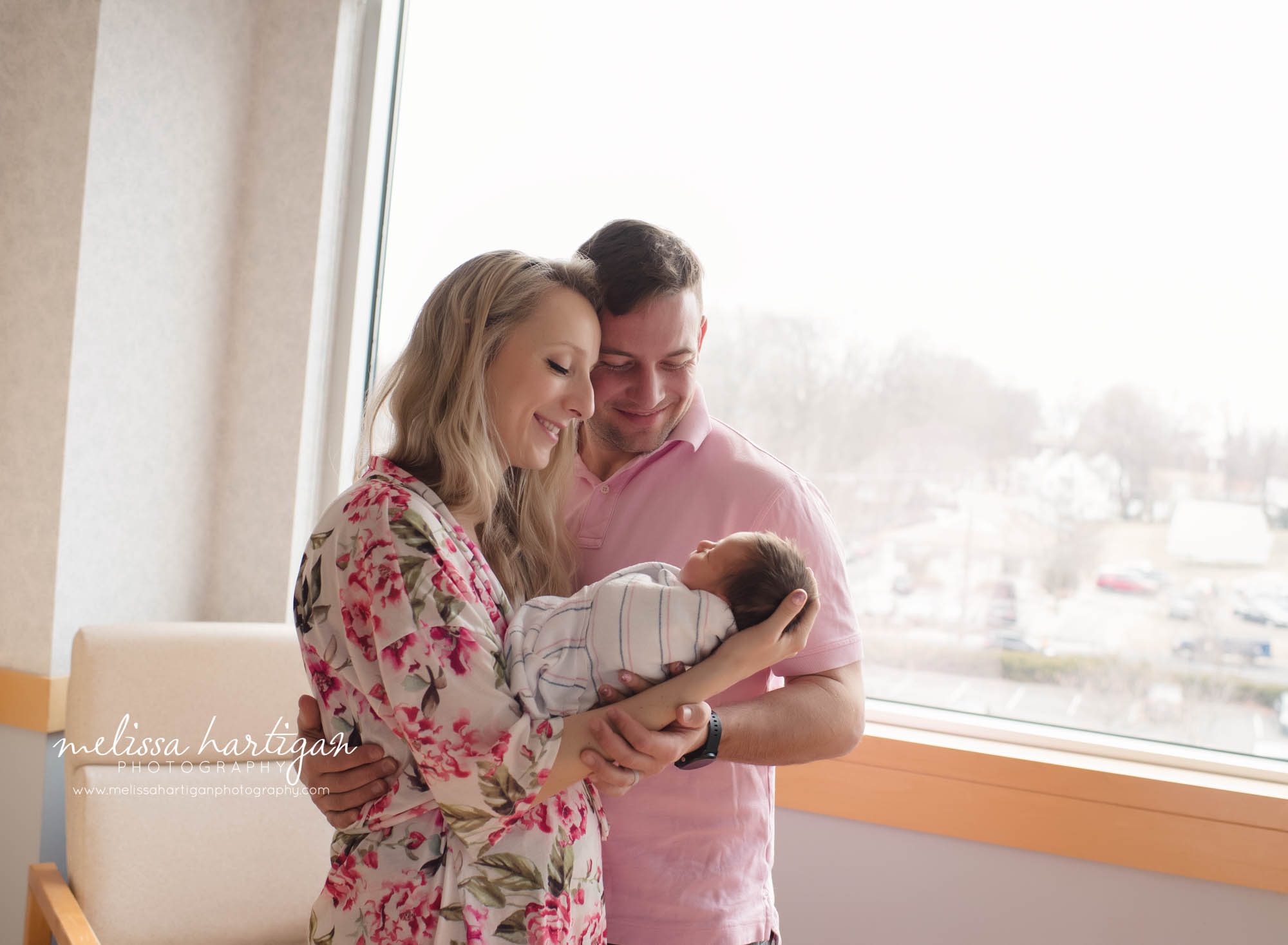 mom dad holding newborn daughter in hospital room postpartum 