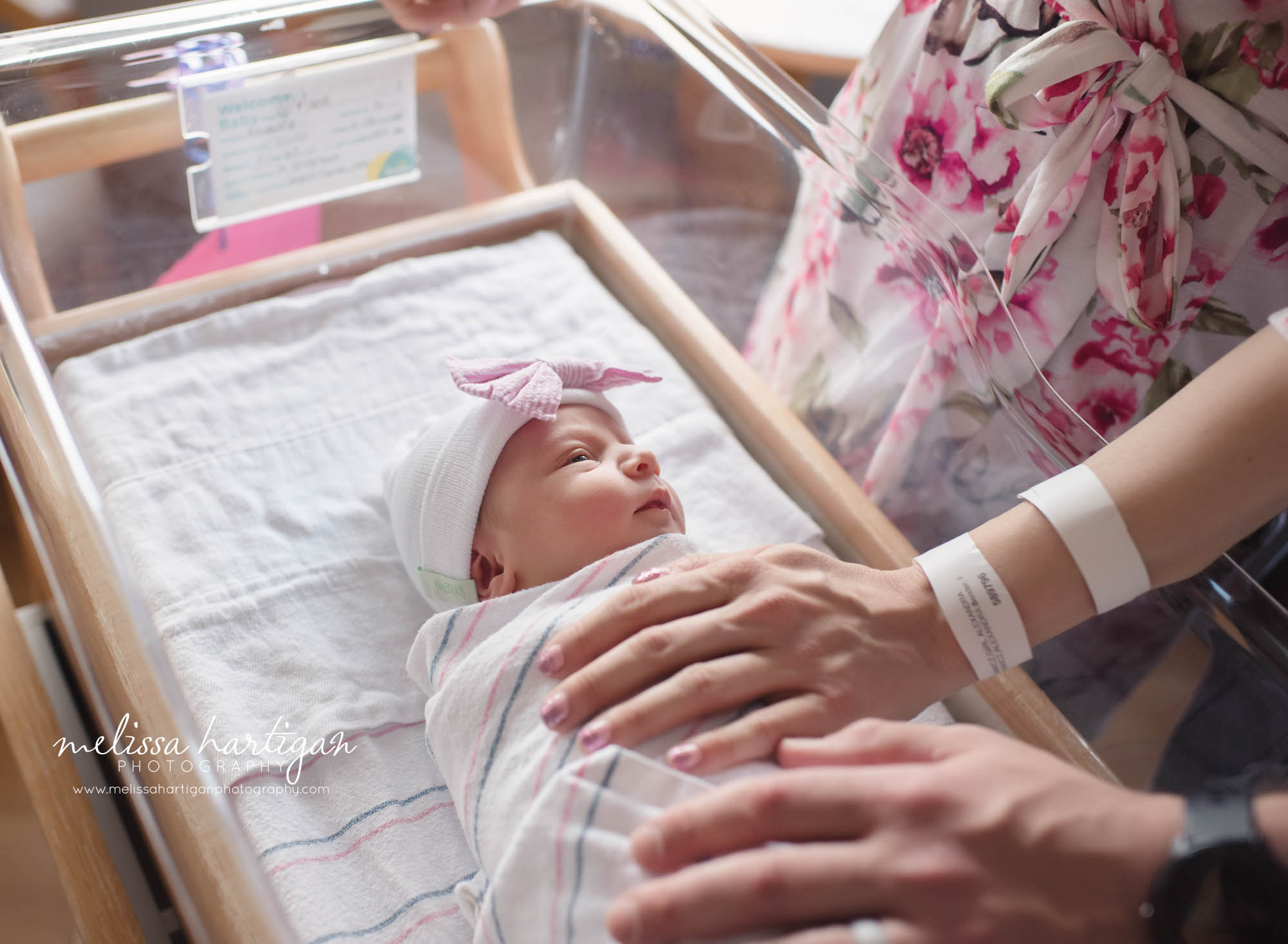 mom and dad holding newborn baby girl laying in hospital bassinet
