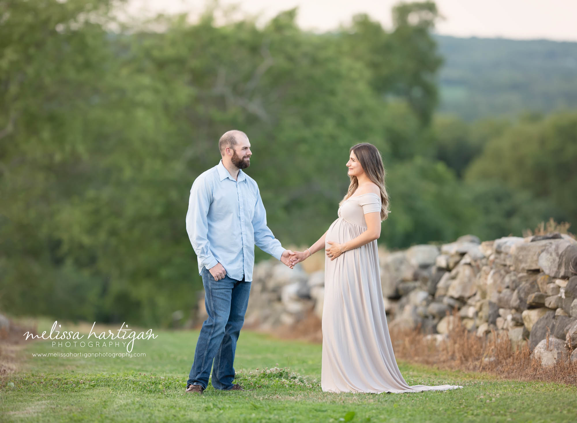 expecti ng couple holding hands looking at each other mom-to-be holding baby bump