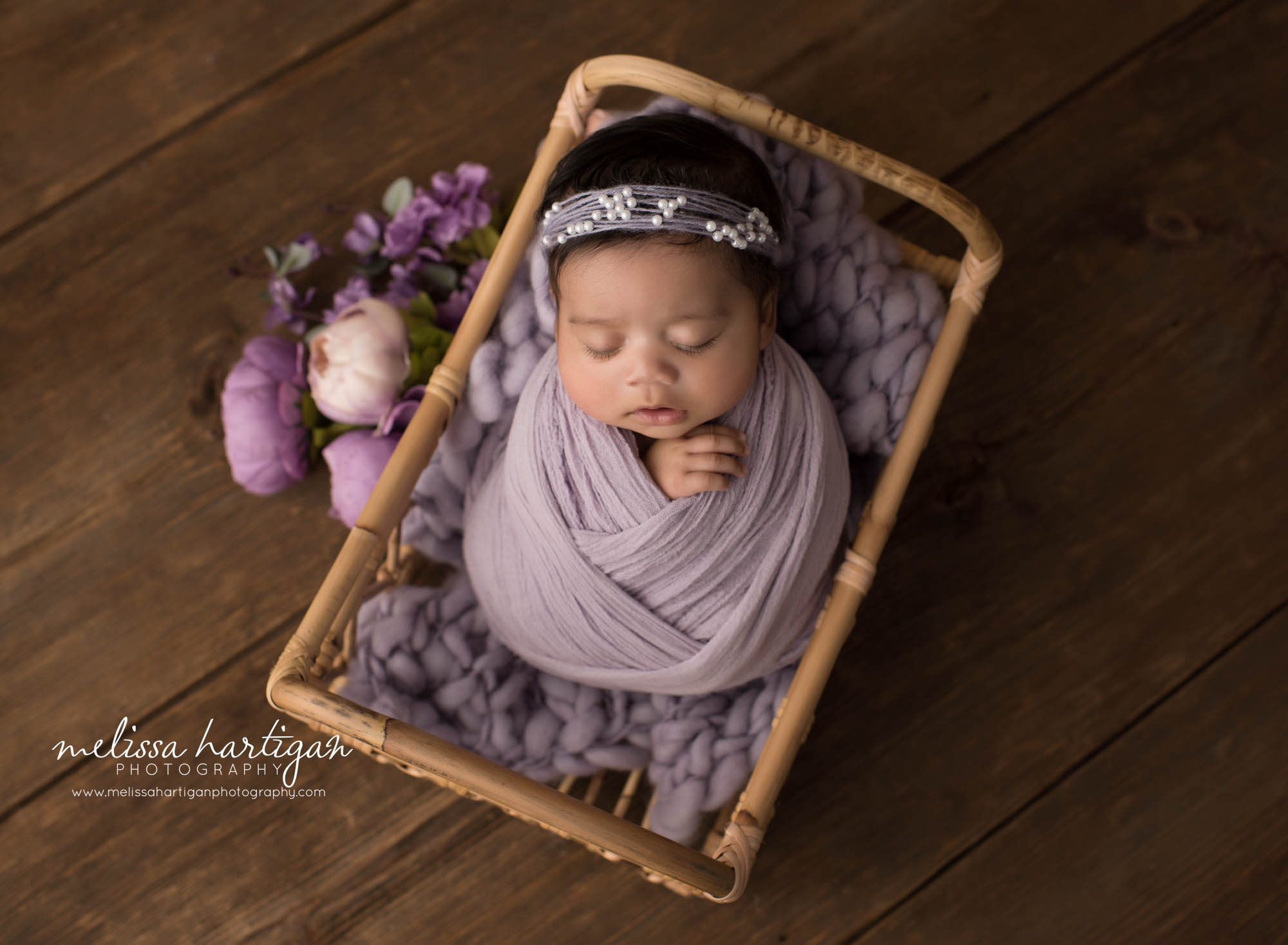 newborn baby girl wrapped in lavendar colored wrap posed in basket