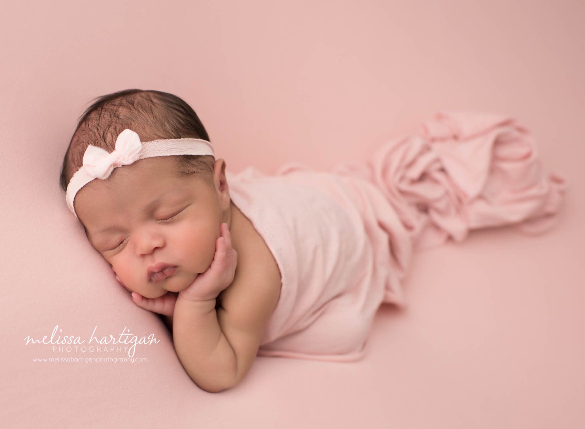 newborn baby girl posed on pink backdrop with pink wrap draped over