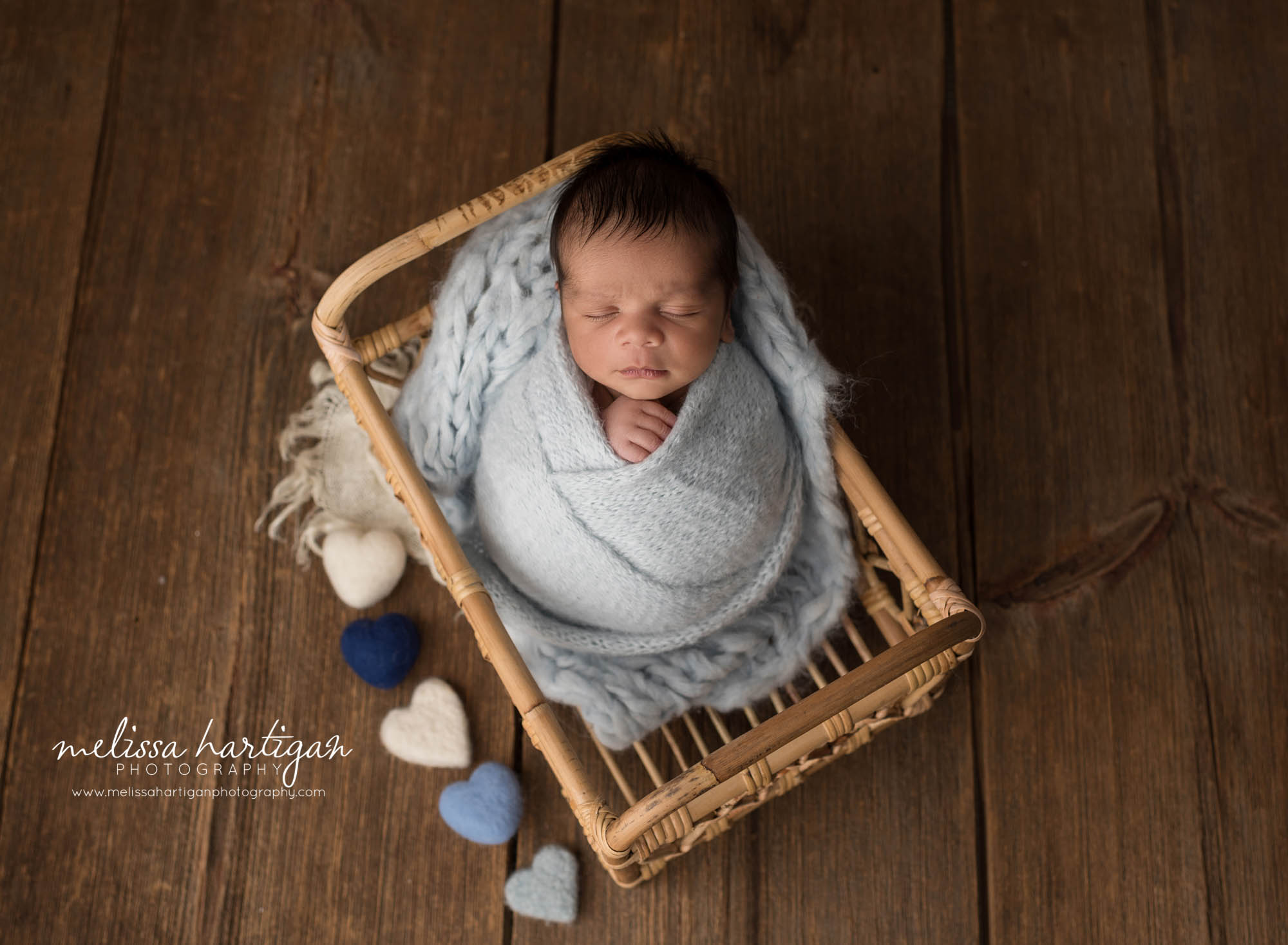 newborn baby boy posed in basket wrapped in knitted light blue layer wrap with blue and cream felted hearts rocky hill newborn photographer