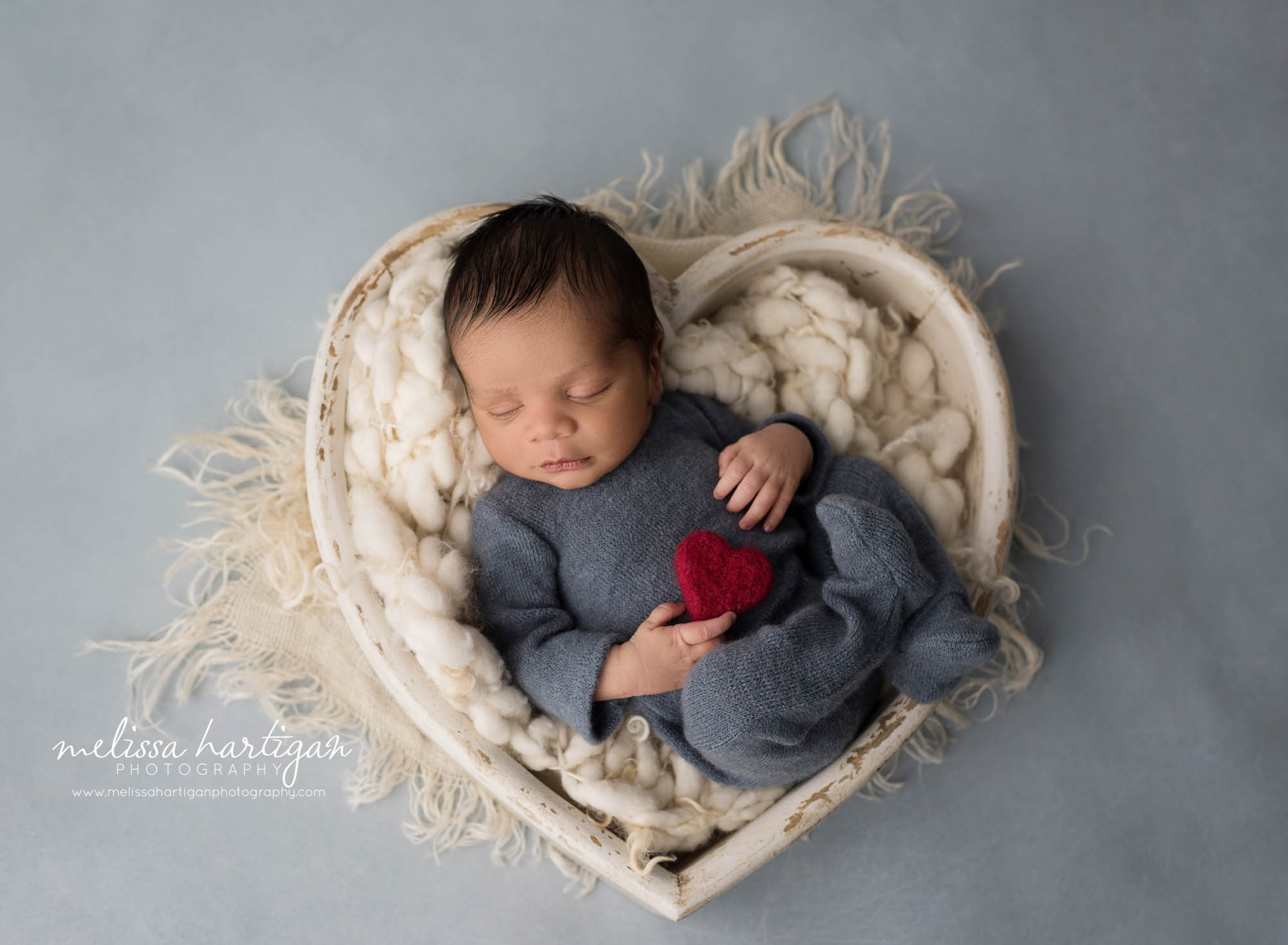 newborn baby boy wearing blue outfit posed cream wooden heart prop holding red felted heart newborn photography rocky hill