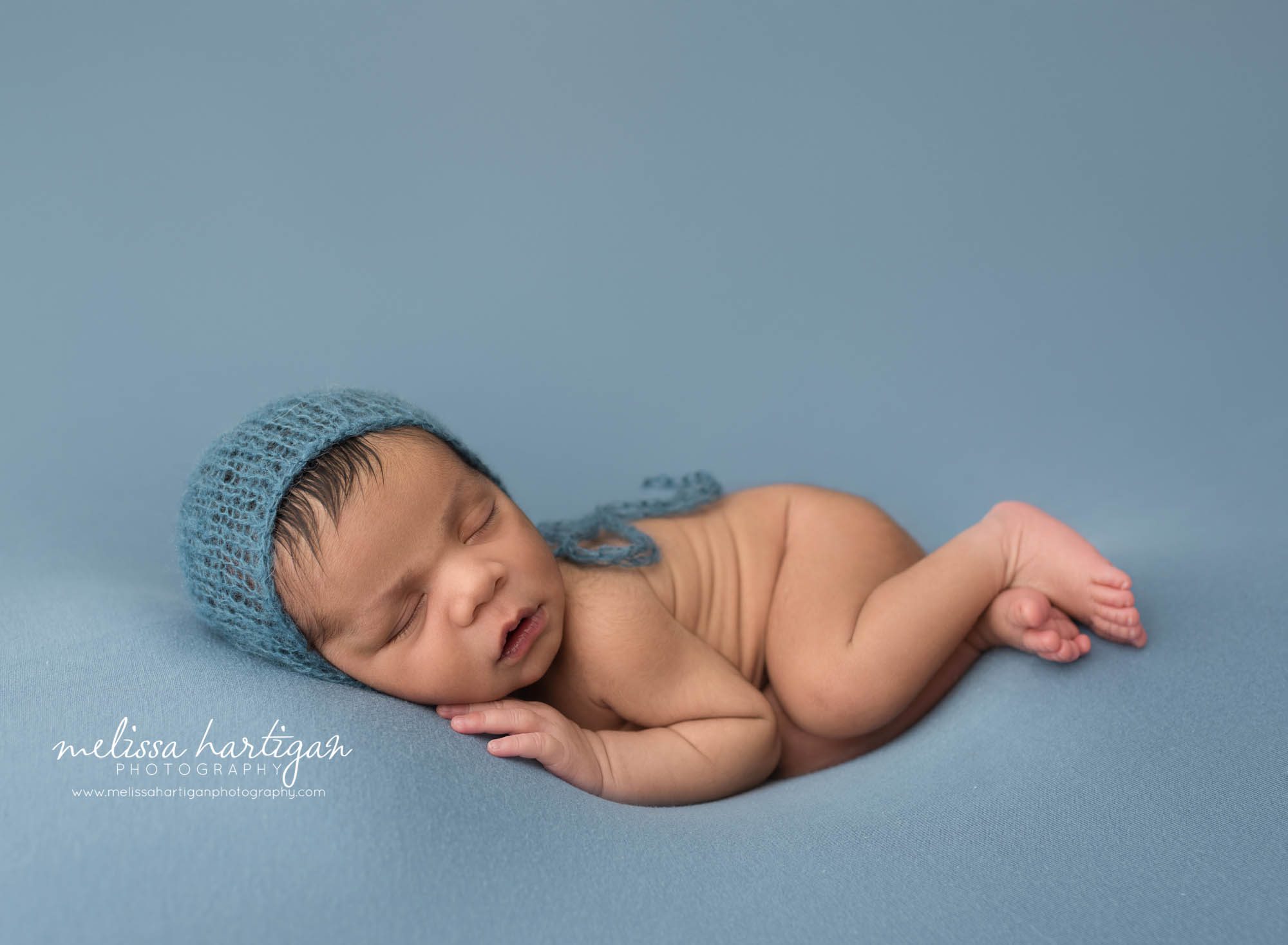 newborn baby boy posed on blue backdrop wearing blue knitted baby bonnet newborn photography rocky hill CT